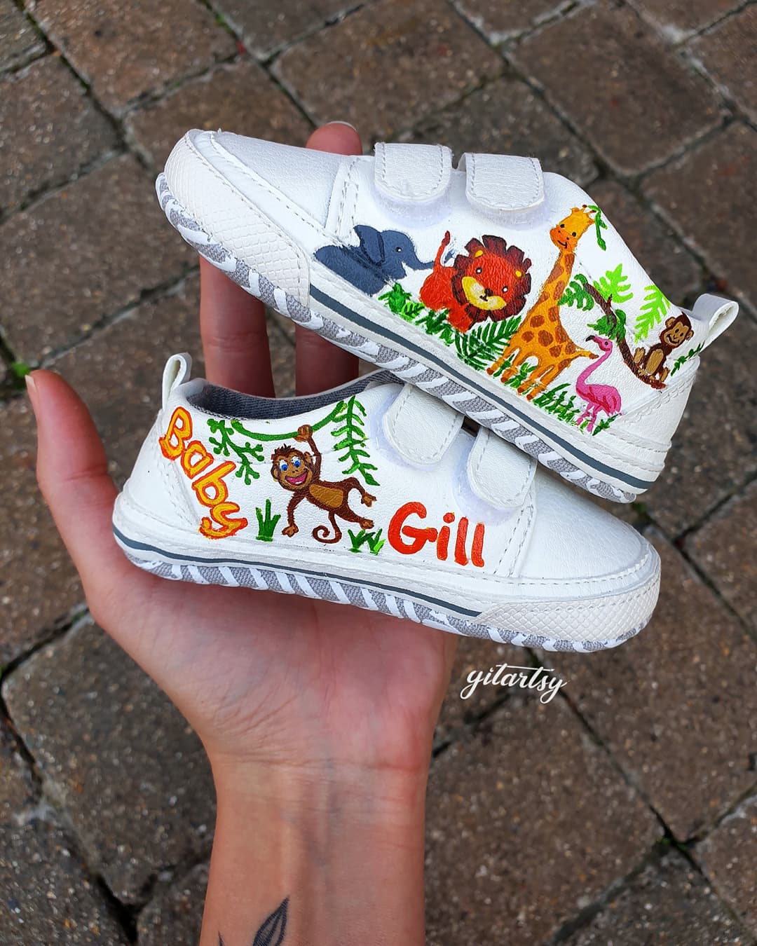 Custom hand-painted sneakers featuring unique artwork of baby animals like giraffes, lions, pandas, and elephants, crafted in vibrant colors and finished with a personalized name such as "Baby Gill". Each pair is a one-of-a-kind creation painted on premium sneakers with waterproof, child-safe materials, ideal for gifting, first birthdays, or keepsakes. The shoes reflect whimsical charm and careful craftsmanship, celebrating childhood through wearable art.