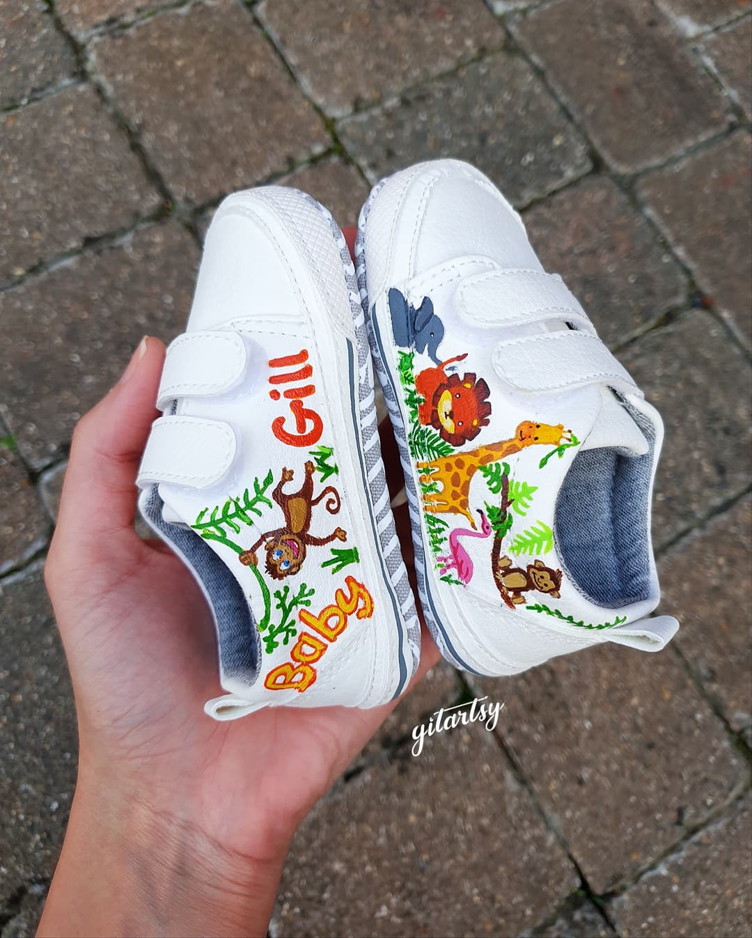 Custom hand-painted sneakers featuring unique artwork of baby animals like giraffes, lions, pandas, and elephants, crafted in vibrant colors and finished with a personalized name such as "Baby Gill". Each pair is a one-of-a-kind creation painted on premium sneakers with waterproof, child-safe materials, ideal for gifting, first birthdays, or keepsakes. The shoes reflect whimsical charm and careful craftsmanship, celebrating childhood through wearable art.