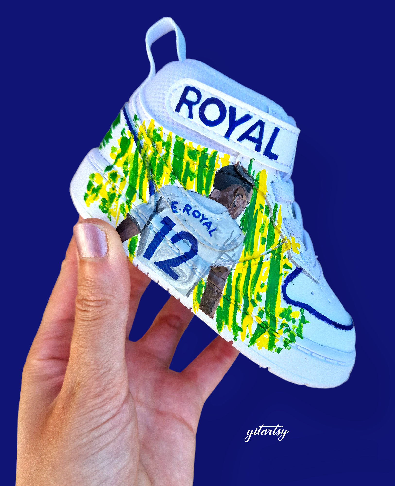 Custom hand-painted baby Adidas sneakers inspired by Brazilian footballer Emerson Royal. Features toddler-sized high-top shoes with illustrations of Emerson in Spurs and Brazil kits, Brazil flag background, colorful 3-stripes, and "Emerson Royal" detailing on the heel. Designed for toddlers, crafted with non-toxic paint, and finished with vibrant detailing by Gitartsy.