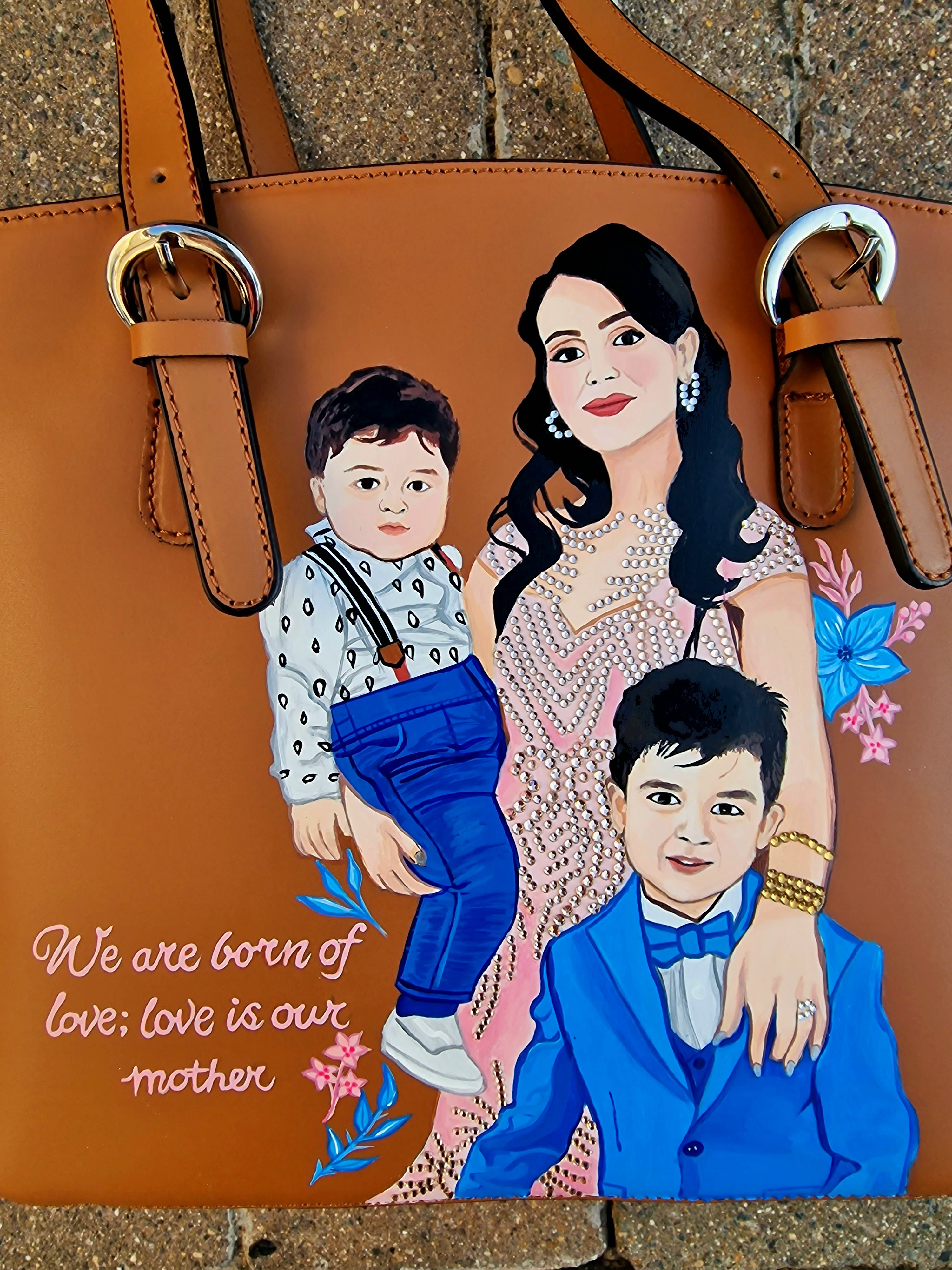 A custom hand-painted tan leather tote bag featuring a family portrait of a mother and two children, designed in a detailed artistic style with floral embellishments and a heartfelt quote. This unique leather bag is personalized from your photos and painted using durable, waterproof paints, ideal as a memory keepsake or meaningful gift for mothers. The painted design stands out against the rich tan leather, making it both functional and sentimental.