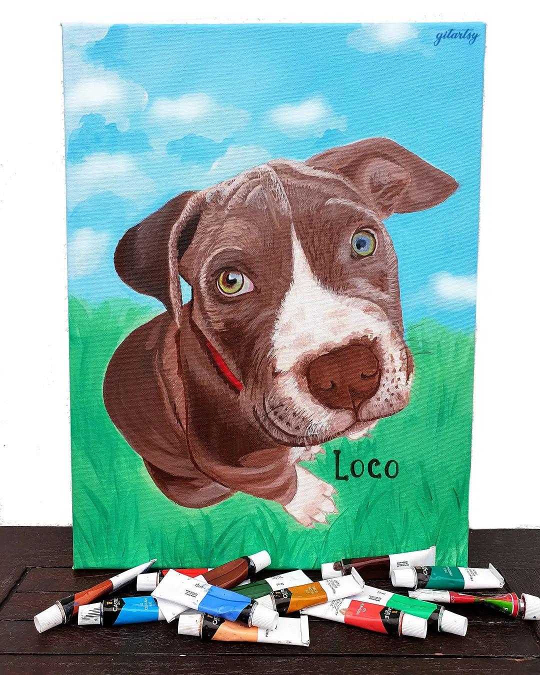 A vibrant hand-painted pet portrait on canvas featuring a detailed, lifelike depiction of a dog with a blue sky and grassy background. The custom artwork showcases a realistic expression and includes the dog’s name, perfect as a sentimental gift or personalized home décor.