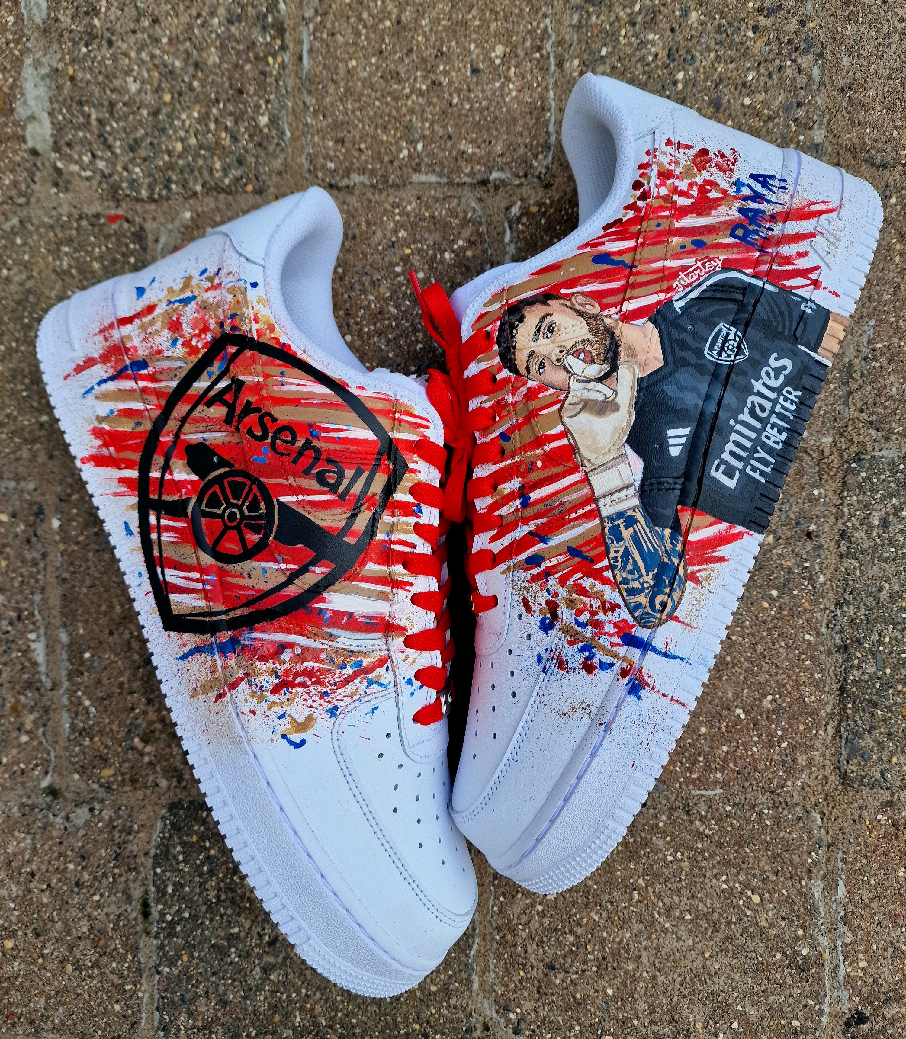 Hand-painted custom Nike Air Force 1 sneakers featuring David Raya in Arsenal goalkeeper kit, Arsenal crest, Spanish flag and colors, vibrant football-inspired splatter artwork, crafted by Gitartsy.