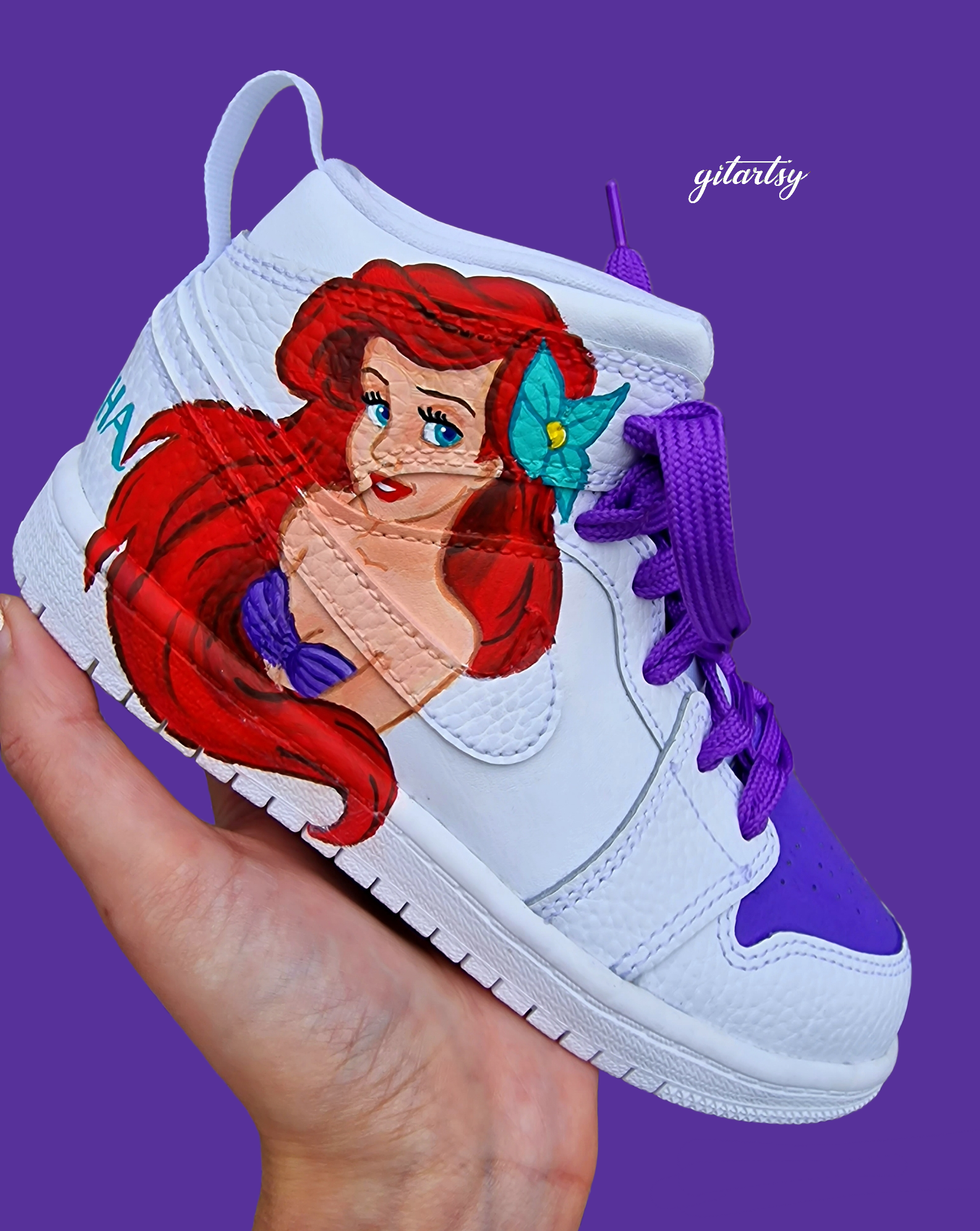 A pair of white Nike toddler sneakers hand-painted with detailed portraits of Disney princesses Jasmine and Ariel. Jasmine is painted in her turquoise outfit with gold accessories, while Ariel is shown with her iconic red hair and purple seashell top. The shoes feature complementary purple and teal accents, vibrant laces, and optional personalised names on the heel in matching colors.