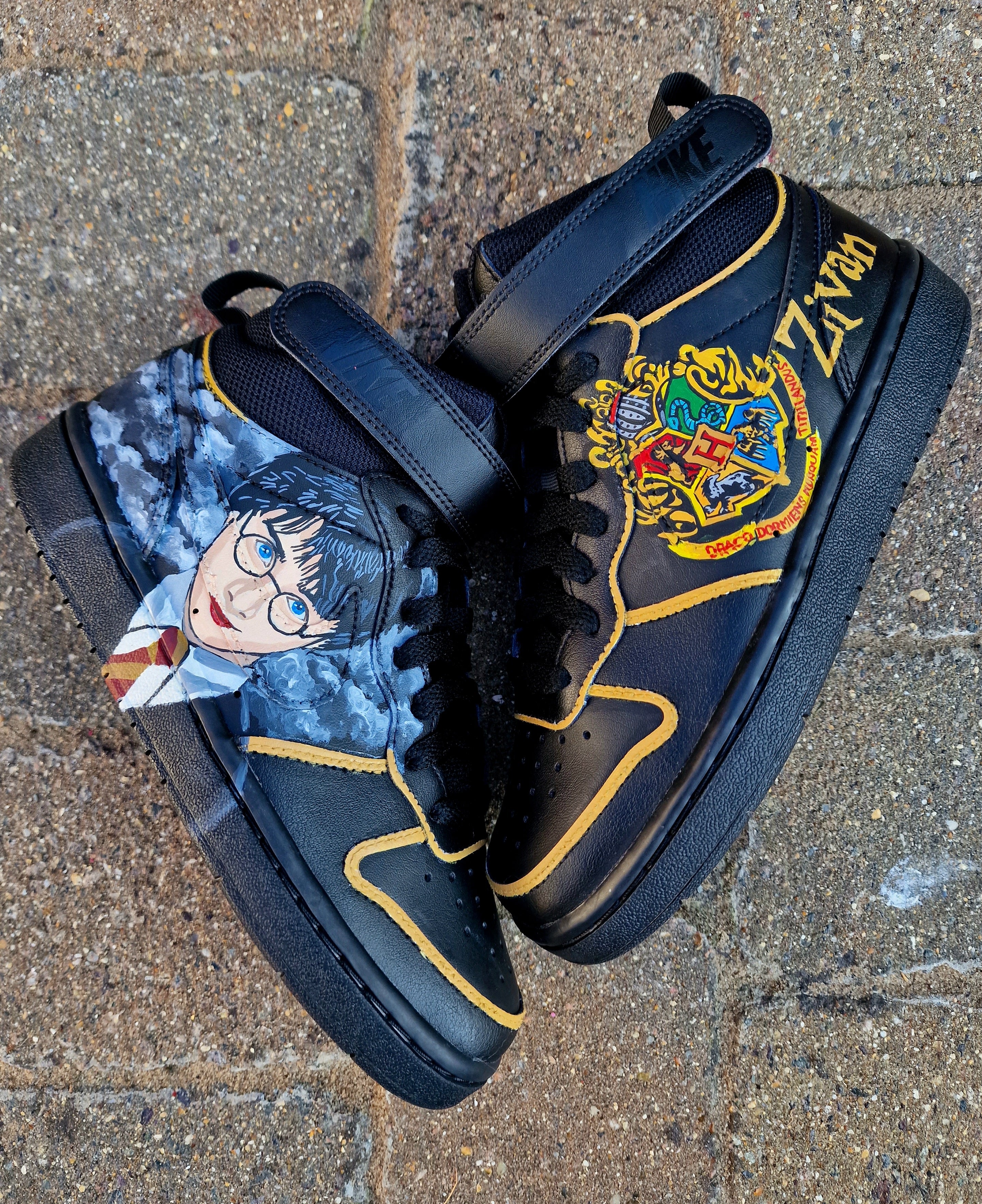 A pair of black Nike AF1 kids sneakers custom hand-painted with a vivid Harry Potter portrait on one side and the colorful Hogwarts Crest on the other, accented with a personalized name in golden lettering. The shoes feature fine detail brushwork, durable waterproof finish, and premium craftsmanship perfect for young Harry Potter fans looking for a magical, unique pair of custom kicks.