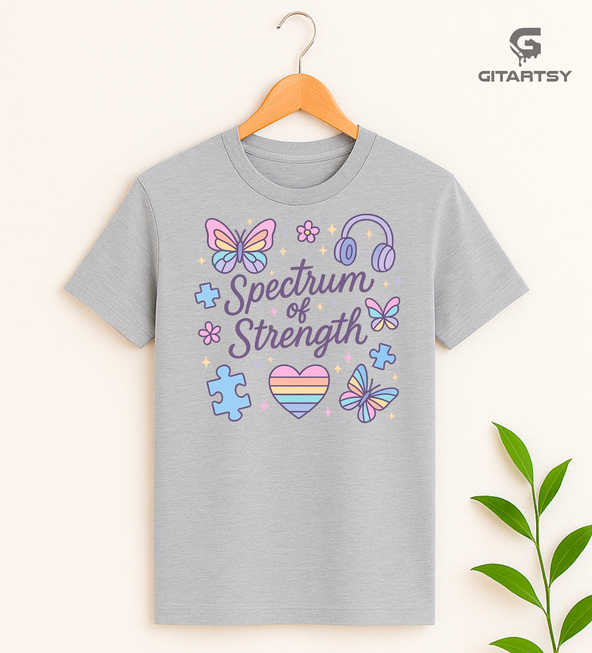 T-shirt with pastel illustrations of butterflies, puzzle pieces, headphones, and the words “Spectrum of Strength”—a positive message celebrating neurodiversity.
