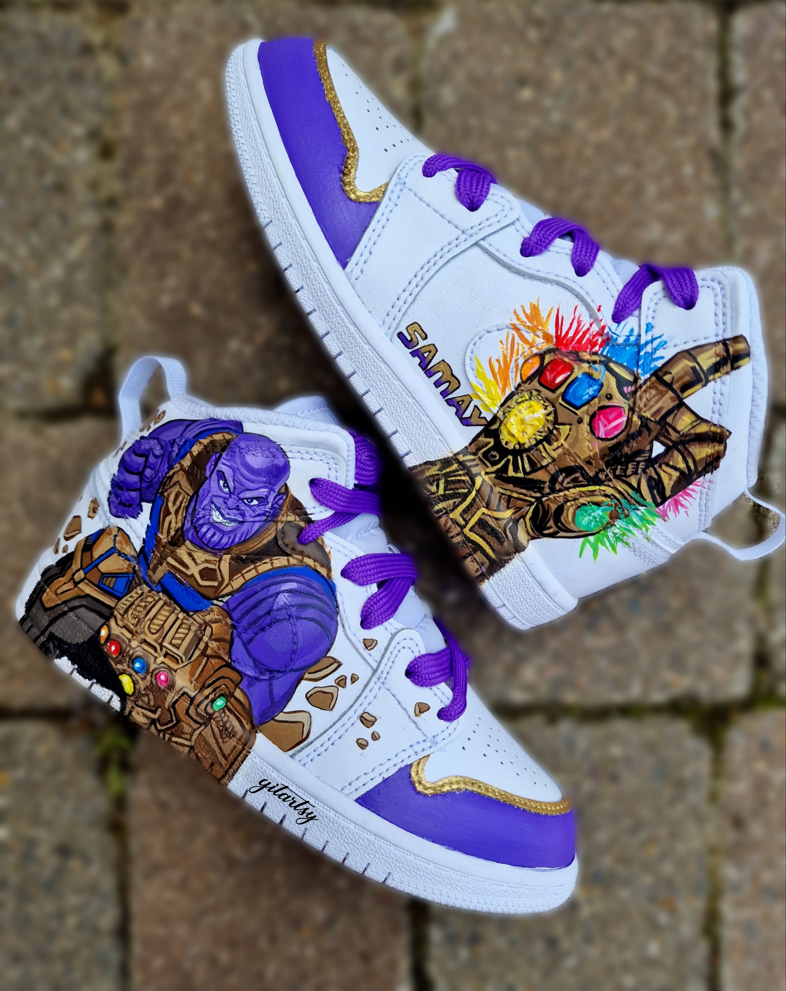 A pair of custom hand-painted kids’ Nike sneakers featuring vibrant comic-inspired designs. One side of the shoes showcases a detailed portrait of a superhero (or villain) with dynamic elements like webs, cosmic effects, or iconic items. The other side includes the child’s personalized name. The colors are bold, the detailing sharp, and the finish protected with a professional-grade sealant for durability. These sneakers combine high-quality craftsmanship with unique customization, making them perfect for s