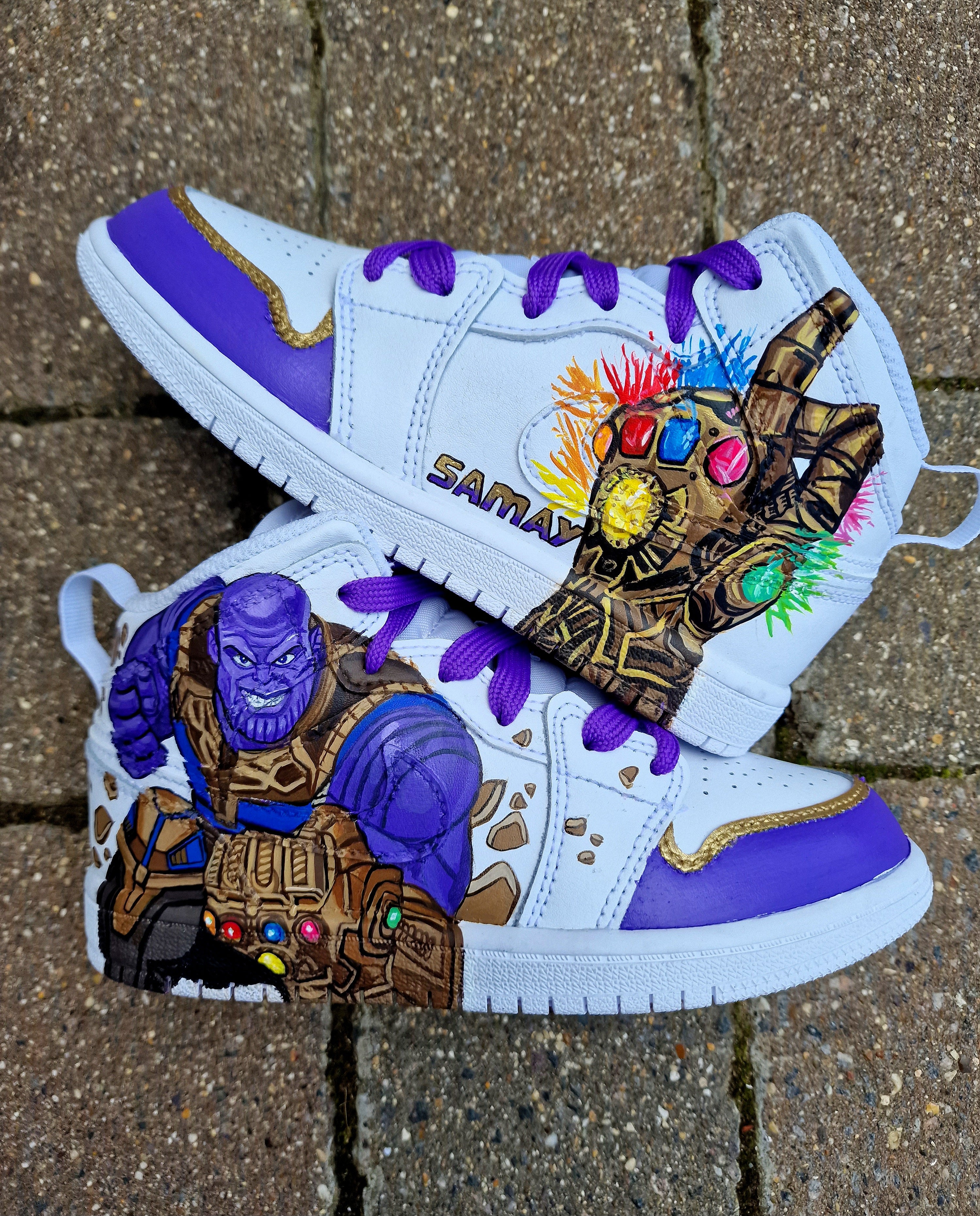 A pair of custom hand-painted kids’ Nike sneakers featuring vibrant comic-inspired designs. One side of the shoes showcases a detailed portrait of a superhero (or villain) with dynamic elements like webs, cosmic effects, or iconic items. The other side includes the child’s personalized name. The colors are bold, the detailing sharp, and the finish protected with a professional-grade sealant for durability. These sneakers combine high-quality craftsmanship with unique customization, making them perfect for s