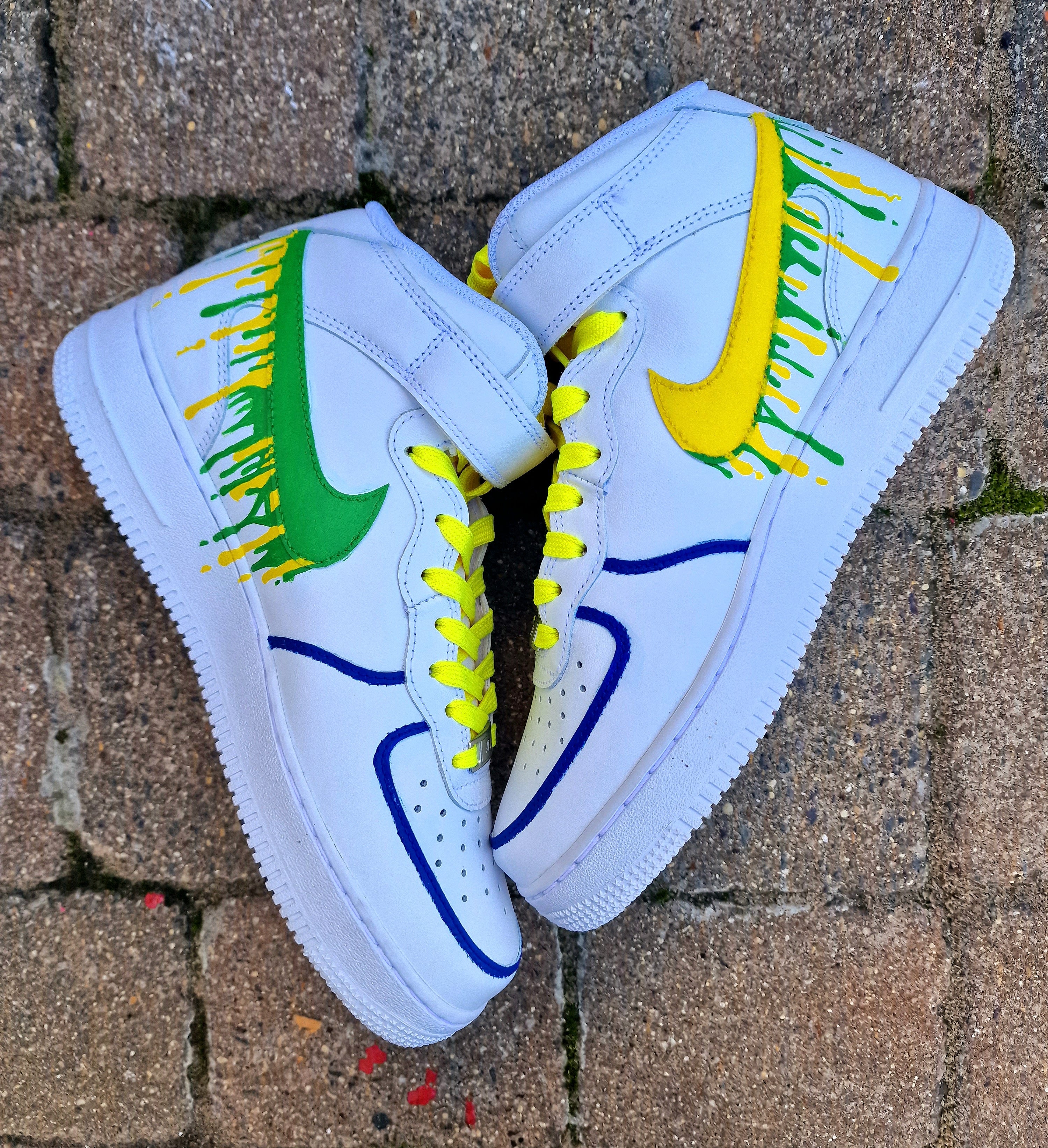 Custom Adolfinho Brazil-inspired Nike Air Force 1 sneakers featuring hand-painted green, yellow, and blue drip art, football graphics, the player name Adolfinho, the number 22, custom strap text, and vivid laces; unique wearable streetwear art designed for football fans and sneaker collectors who want personalised, one-of-a-kind kicks that celebrate Brazilian sports culture.