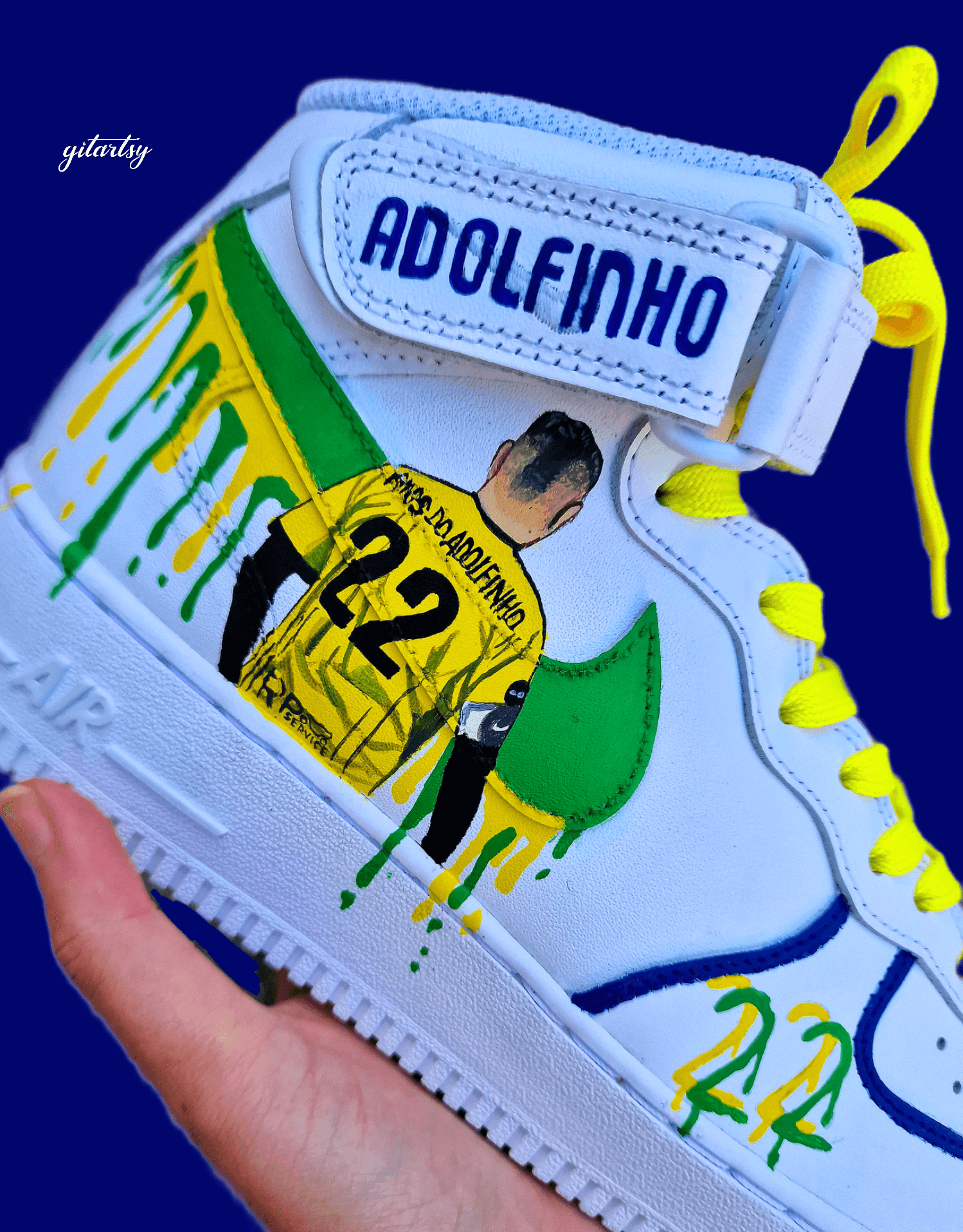 Custom Adolfinho Brazil-inspired Nike Air Force 1 sneakers featuring hand-painted green, yellow, and blue drip art, football graphics, the player name Adolfinho, the number 22, custom strap text, and vivid laces; unique wearable streetwear art designed for football fans and sneaker collectors who want personalised, one-of-a-kind kicks that celebrate Brazilian sports culture.