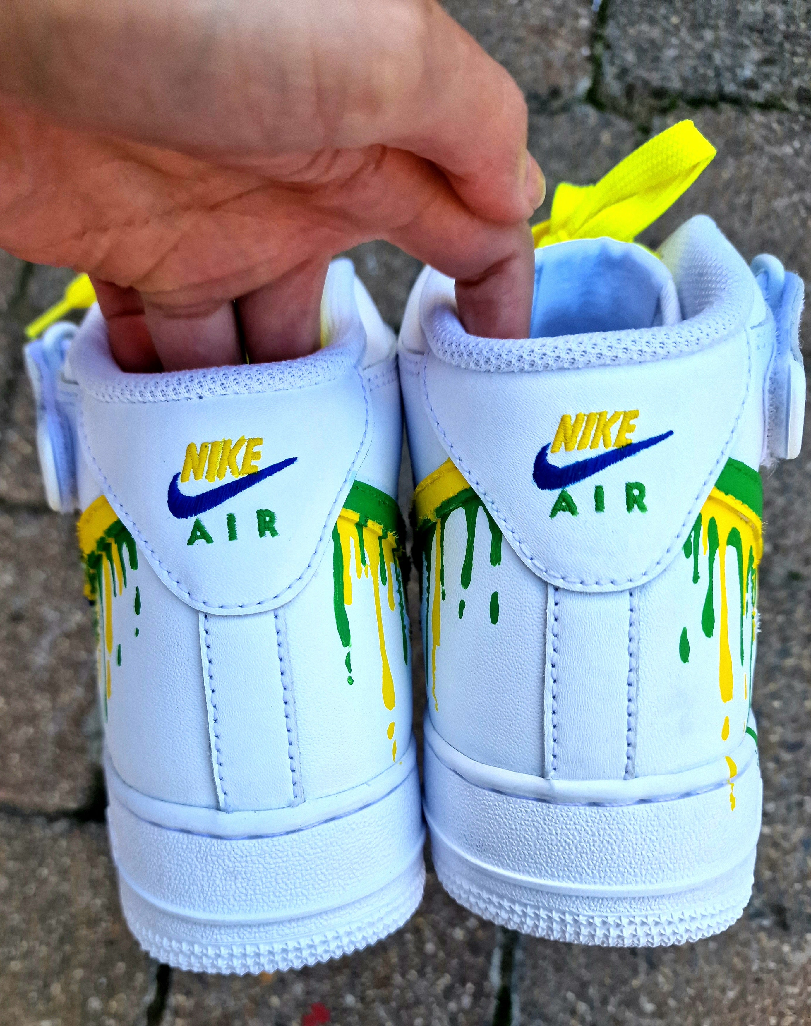 Custom Adolfinho Brazil-inspired Nike Air Force 1 sneakers featuring hand-painted green, yellow, and blue drip art, football graphics, the player name Adolfinho, the number 22, custom strap text, and vivid laces; unique wearable streetwear art designed for football fans and sneaker collectors who want personalised, one-of-a-kind kicks that celebrate Brazilian sports culture.