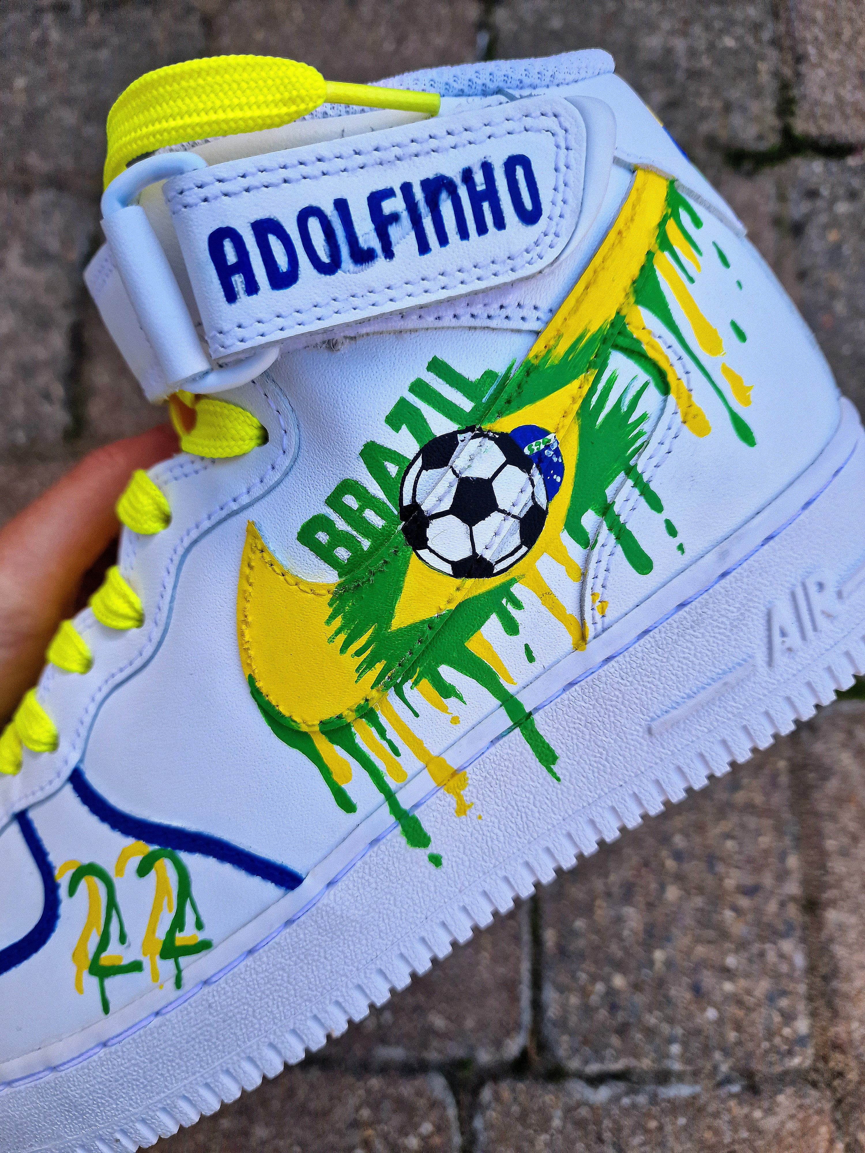 Custom Adolfinho Brazil-inspired Nike Air Force 1 sneakers featuring hand-painted green, yellow, and blue drip art, football graphics, the player name Adolfinho, the number 22, custom strap text, and vivid laces; unique wearable streetwear art designed for football fans and sneaker collectors who want personalised, one-of-a-kind kicks that celebrate Brazilian sports culture.