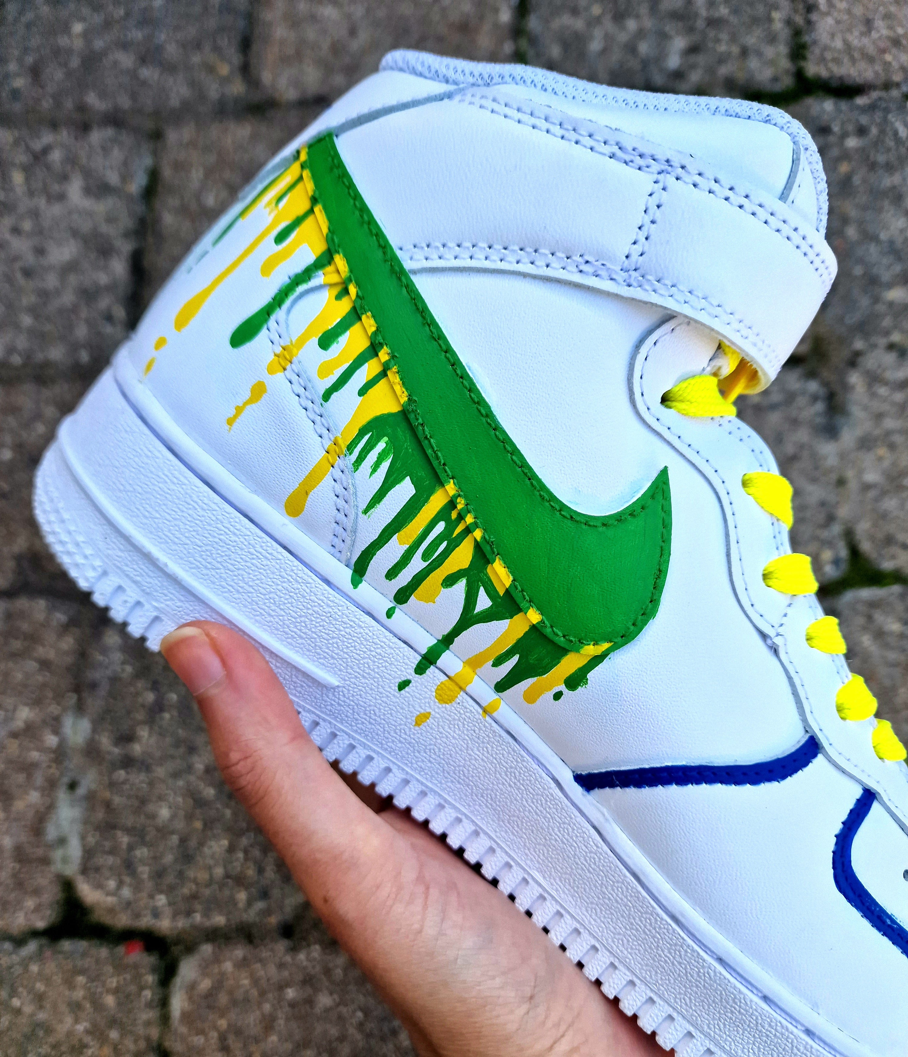 Custom Adolfinho Brazil-inspired Nike Air Force 1 sneakers featuring hand-painted green, yellow, and blue drip art, football graphics, the player name Adolfinho, the number 22, custom strap text, and vivid laces; unique wearable streetwear art designed for football fans and sneaker collectors who want personalised, one-of-a-kind kicks that celebrate Brazilian sports culture.