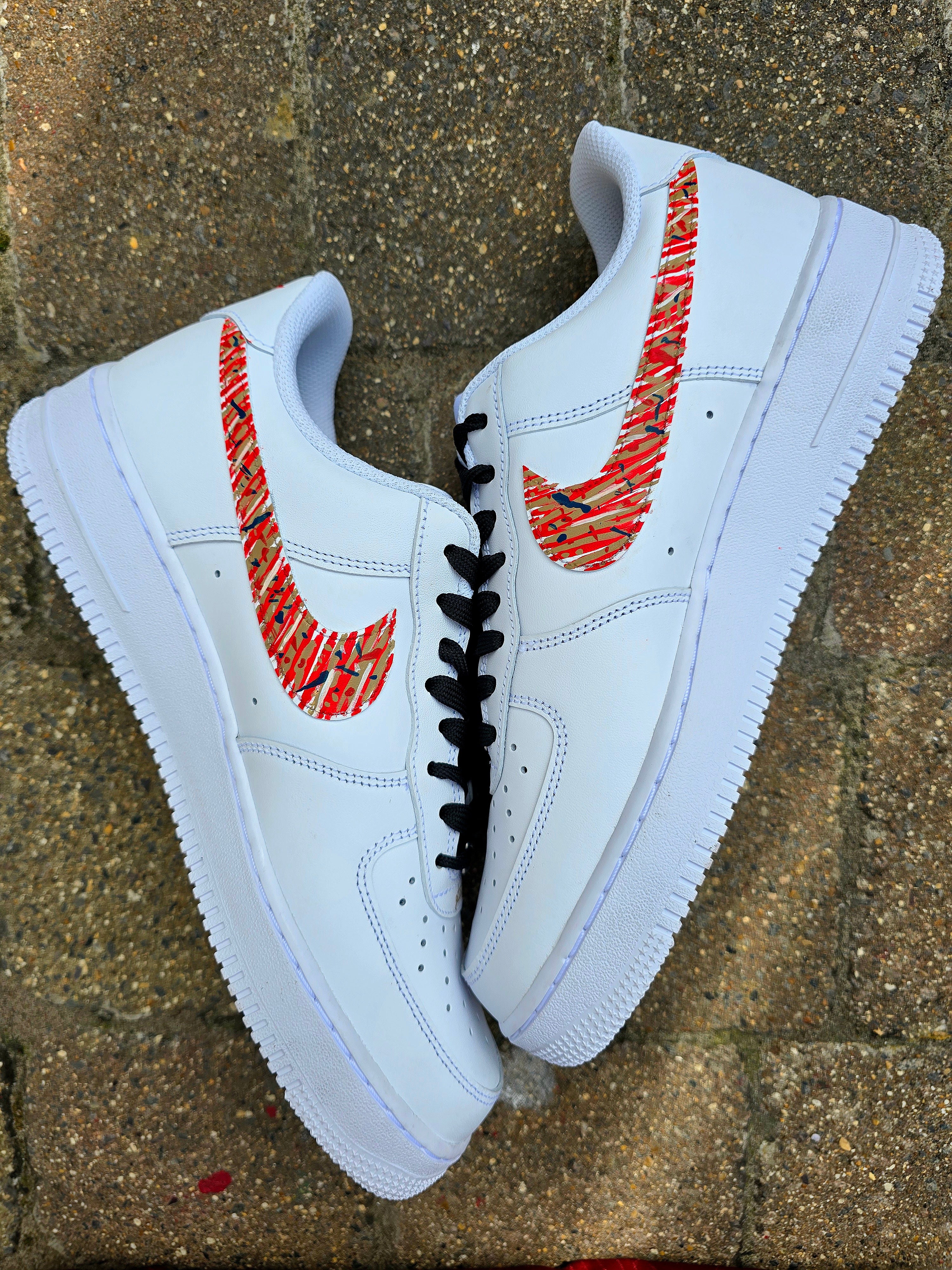 Custom hand-painted Nike Air Force 1 sneakers with Arsenal FC-inspired design, featuring red, gold, and navy brush strokes, personalized details like player name and number, Arsenal logo, and splatter effect art—crafted on a genuine white leather Nike AF1 base by Gitartsy.

