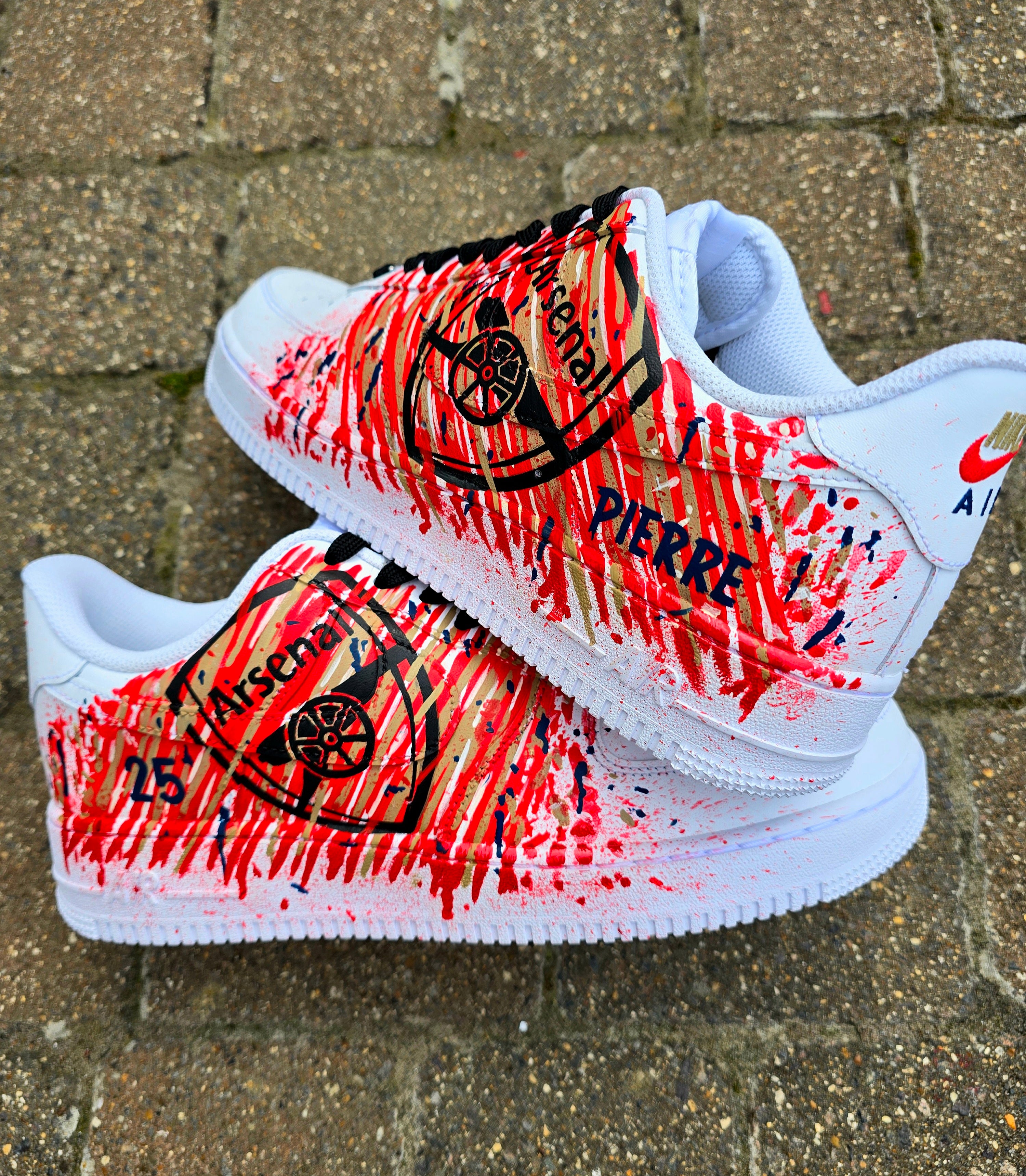 Custom hand-painted Nike Air Force 1 sneakers with Arsenal FC-inspired design, featuring red, gold, and navy brush strokes, personalized details like player name and number, Arsenal logo, and splatter effect art—crafted on a genuine white leather Nike AF1 base by Gitartsy.

