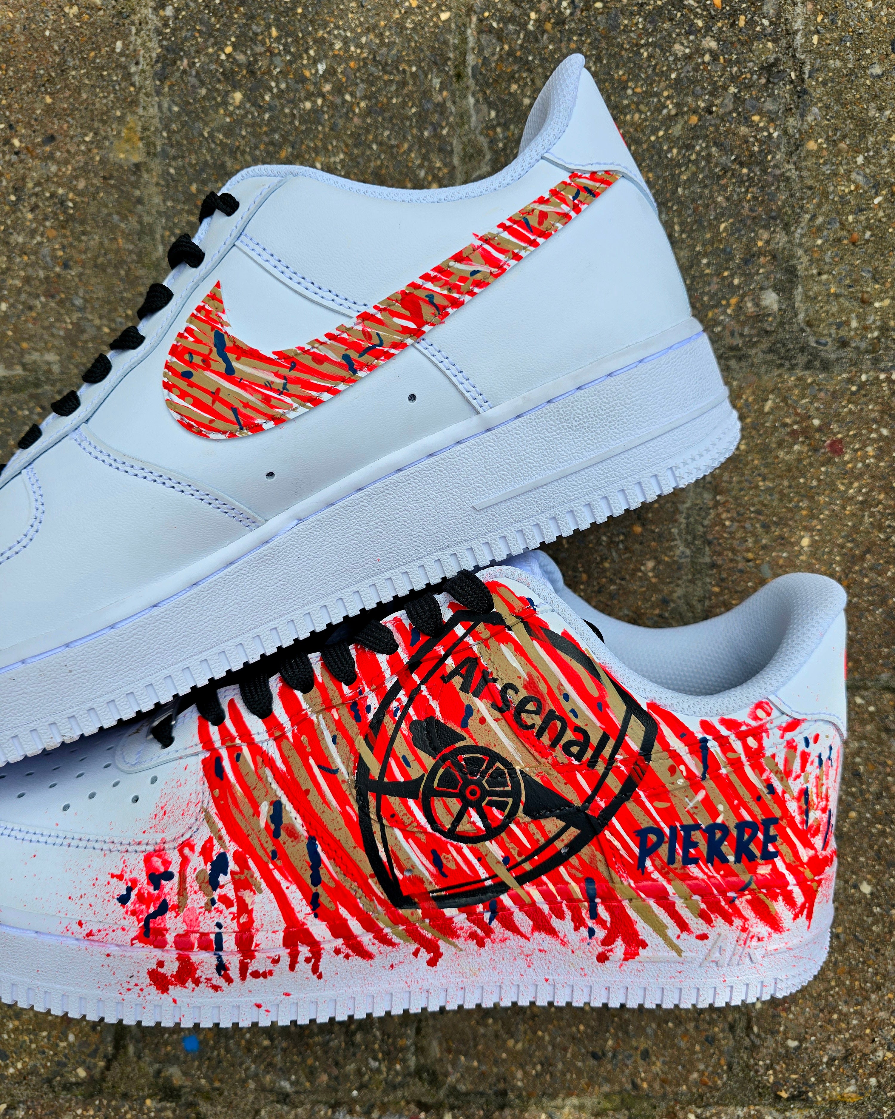 Custom hand-painted Nike Air Force 1 sneakers with Arsenal FC-inspired design, featuring red, gold, and navy brush strokes, personalized details like player name and number, Arsenal logo, and splatter effect art—crafted on a genuine white leather Nike AF1 base by Gitartsy.

