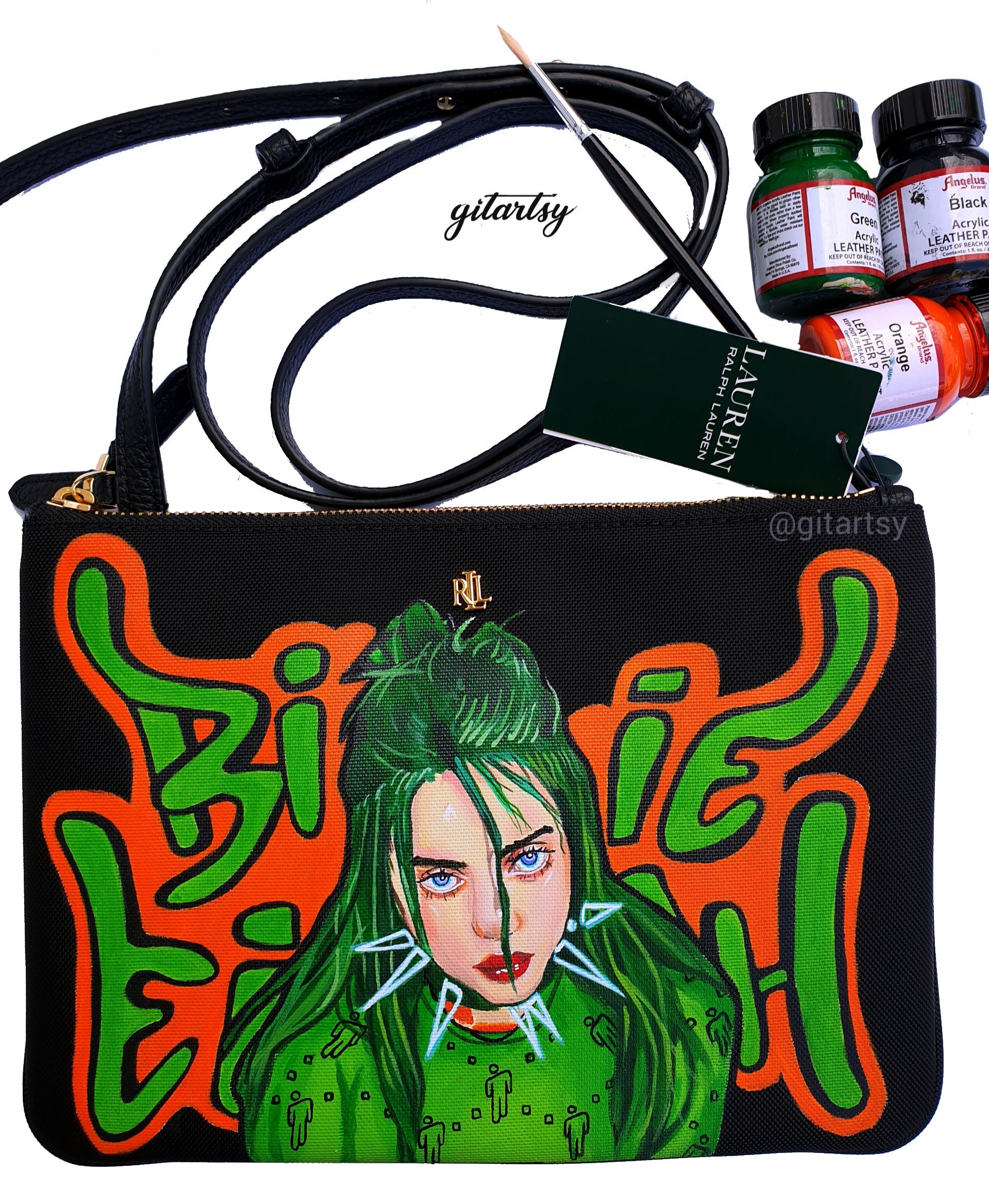 A black Ralph Lauren crossbody canvas bag with a vivid hand-painted portrait of Billie Eilish featuring neon green hair and piercing blue eyes. Surrounding her are graffiti-style green and orange letters spelling “Billie Eilish”. The bag includes a sleek black strap and gold Ralph Lauren logo detailing. High-quality acrylic leather paints are shown in the background alongside a fine detail paintbrush, highlighting the hand-painted craftsmanship.