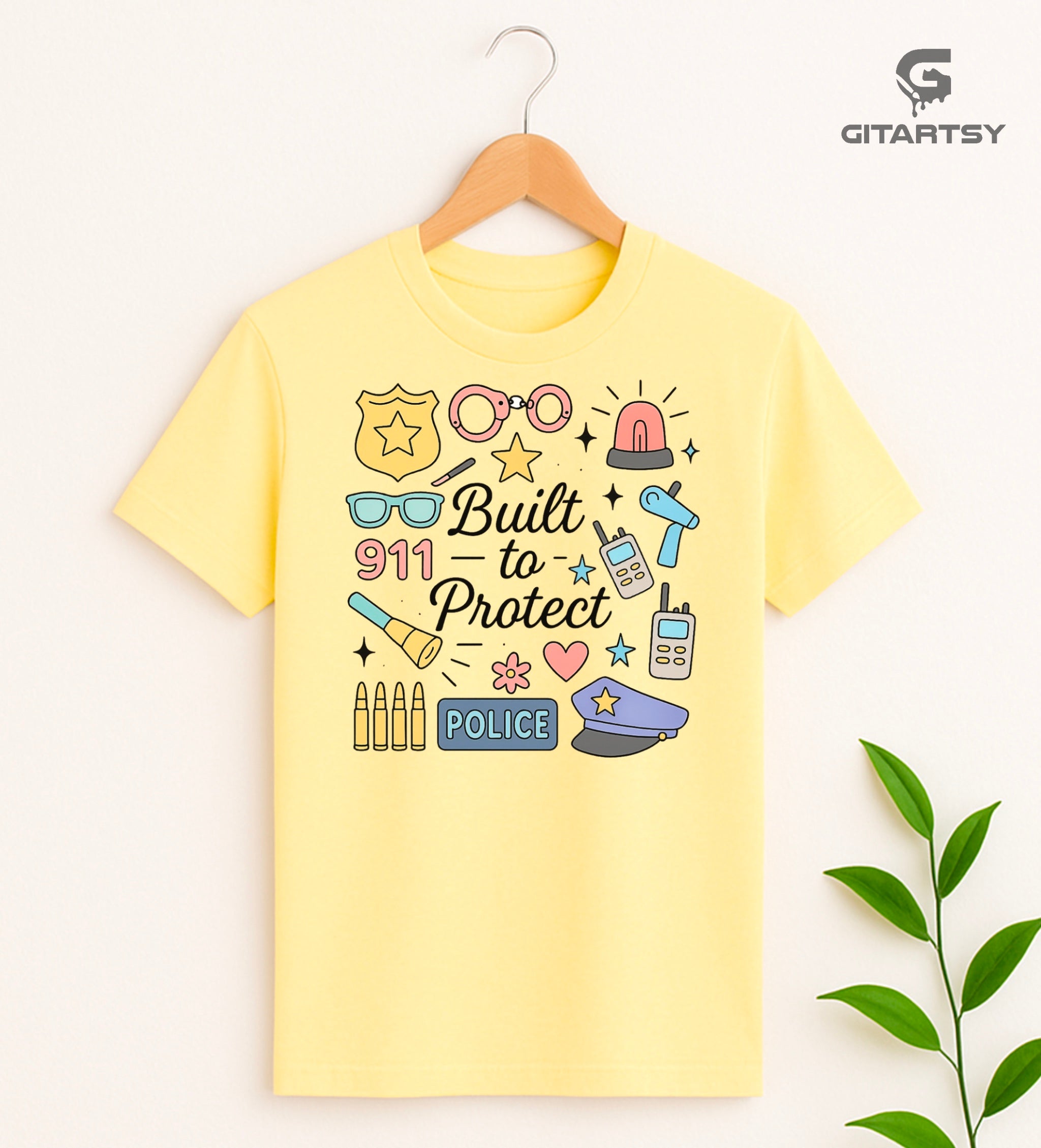 Pastel graphic T-shirt for policewomen with icons like badges, handcuffs, sirens, and 911 – “Built to Protect” slogan in stylish typography.