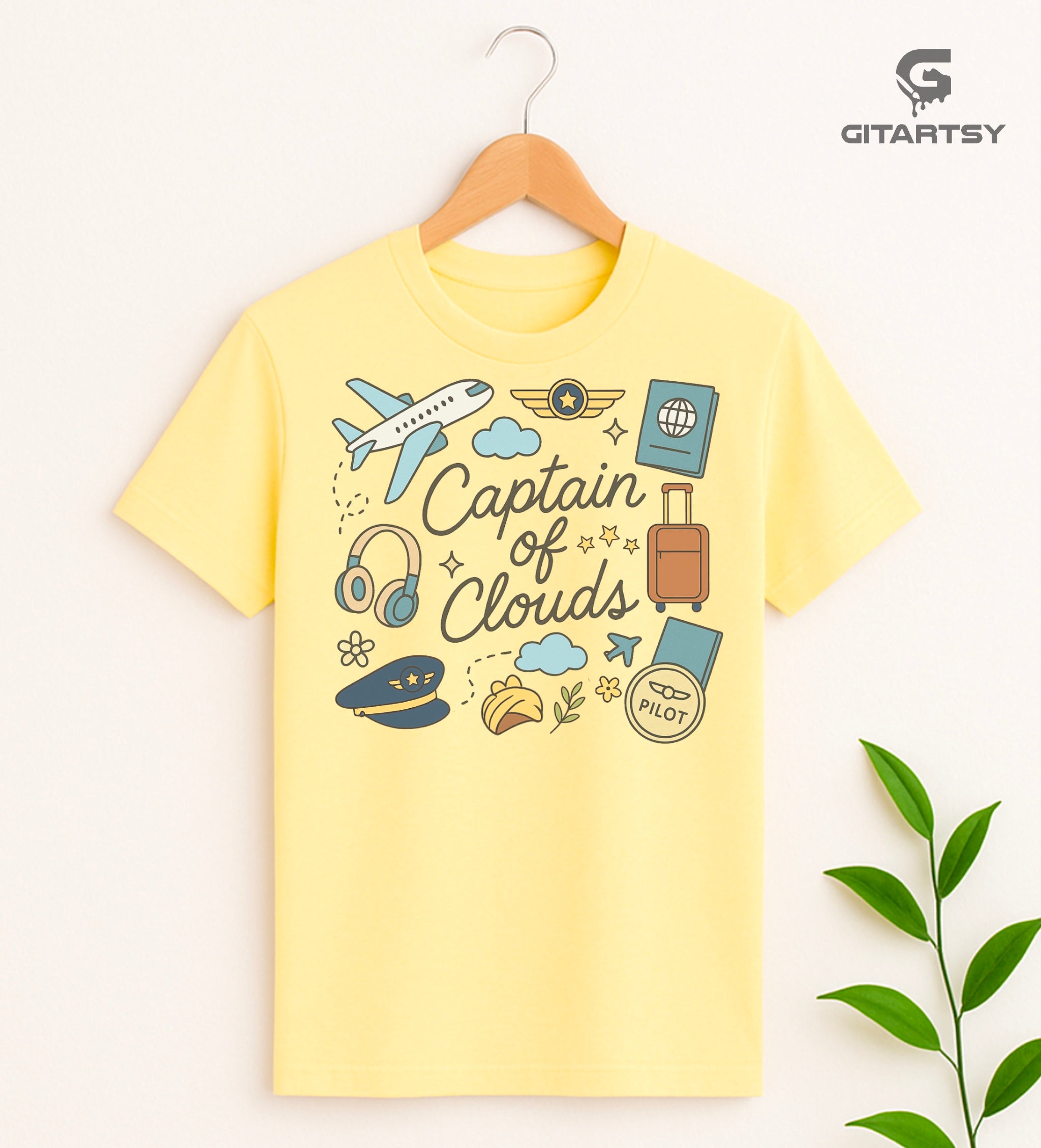 Pastel pilot-themed t-shirt with plane, cloud, headset, and travel icons. "Captain of Clouds" design for aviation lovers and airline crew.