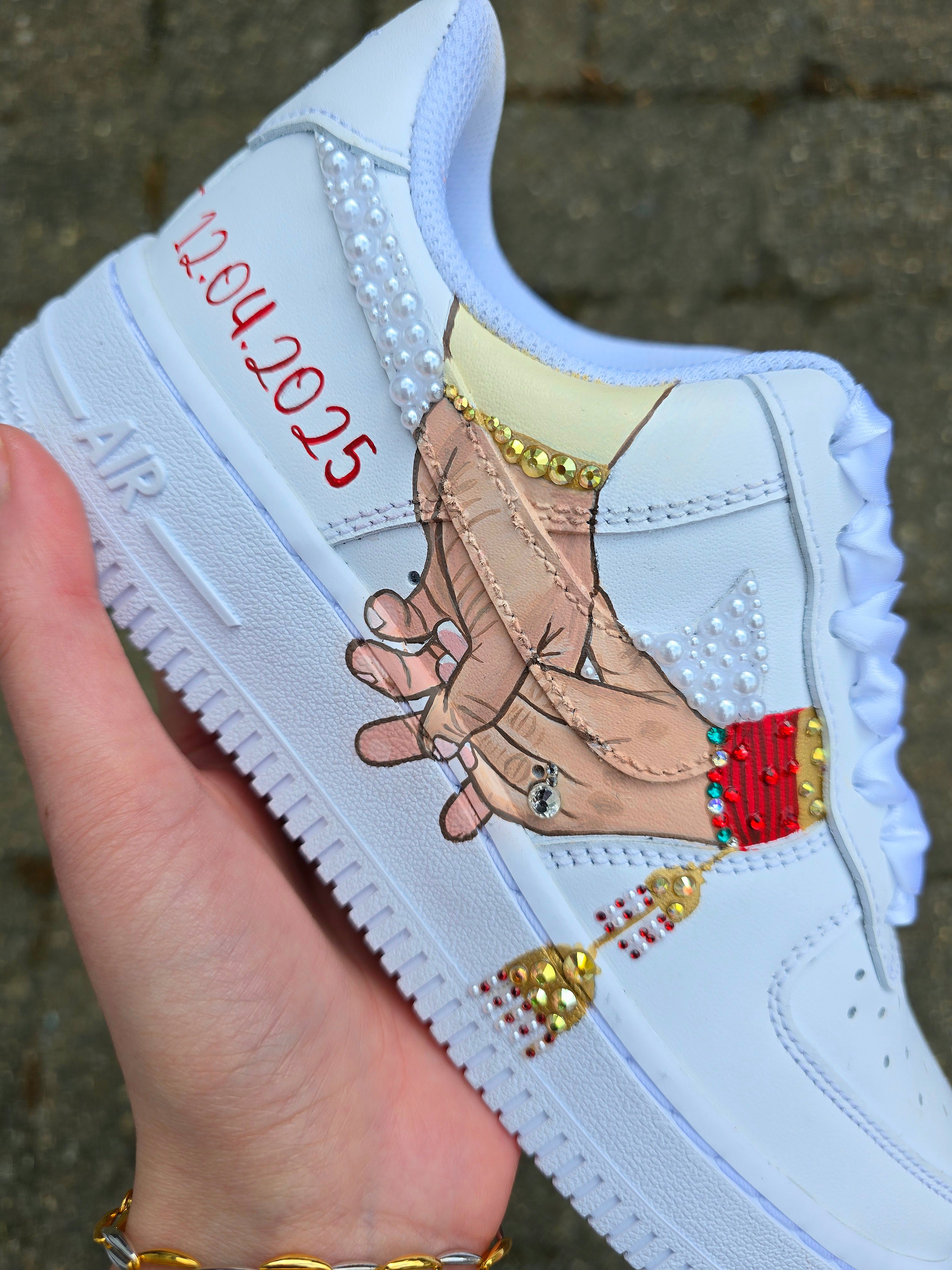 Custom Nike Air Force 1 sneakers hand-painted with a realistic bride and groom portrait, wedding attire details, and personalised touches such as names and dates. Embellished with pearls, rhinestones, and gold accents, these sneakers feature intricate artwork depicting the couple in formal wear and symbolic wedding imagery like clasped hands. Crafted with professional-grade leather paints and sealed for long-lasting wear, these wedding edition shoes combine comfort, style, and sentimental value.

