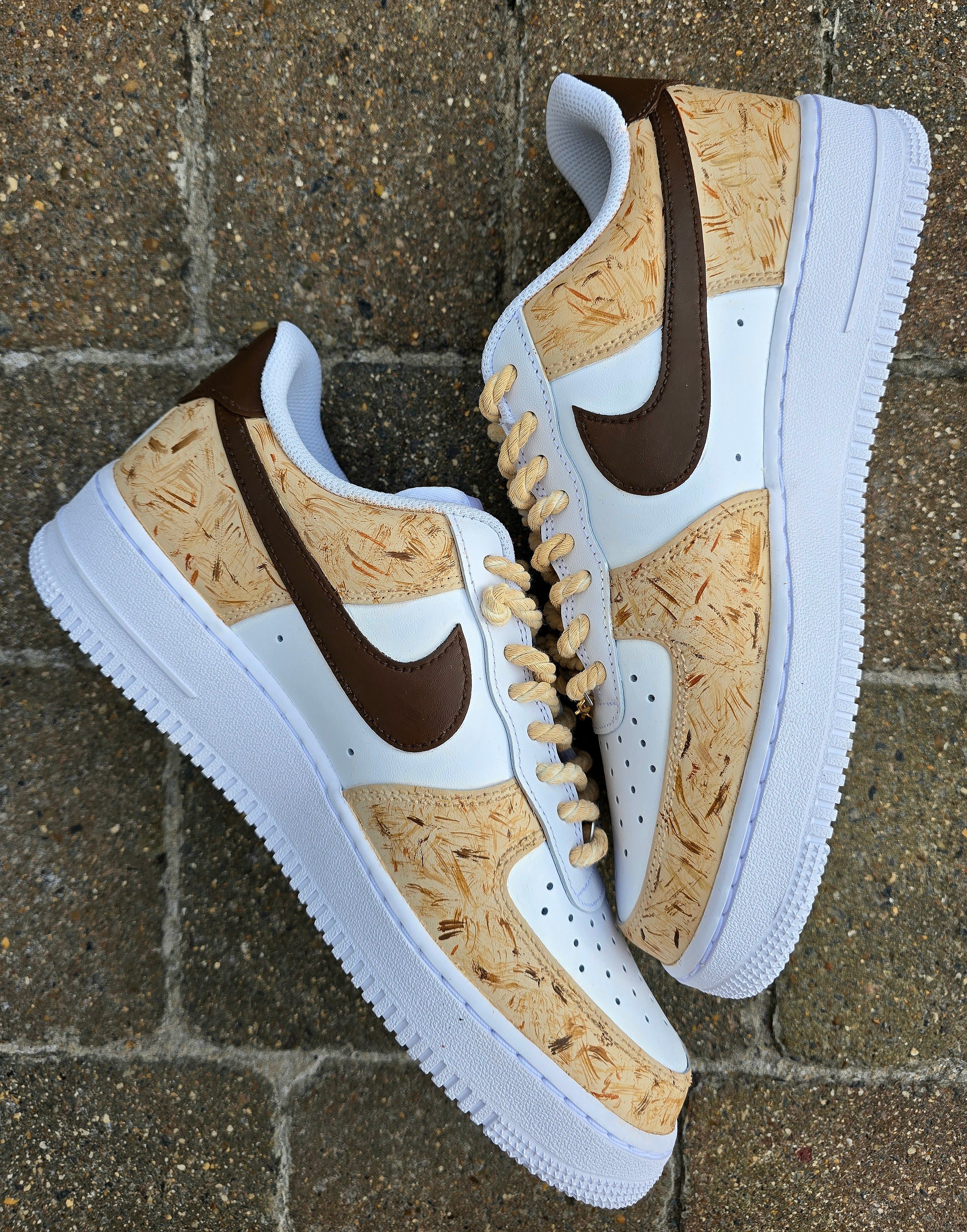 Custom hand-painted Nike Air Force 1 sneakers featuring a detailed portrait of a fluffy brown dog named Poppy 🐶. The shoes have a white leather base with light brown textured paint accents and a rich chocolate-brown swoosh adorned with paw prints 🐾. The pet’s name is written in a playful font, and tan rope laces add a rustic touch. Perfect for showcasing love for your pet in a stylish and artistic way.

