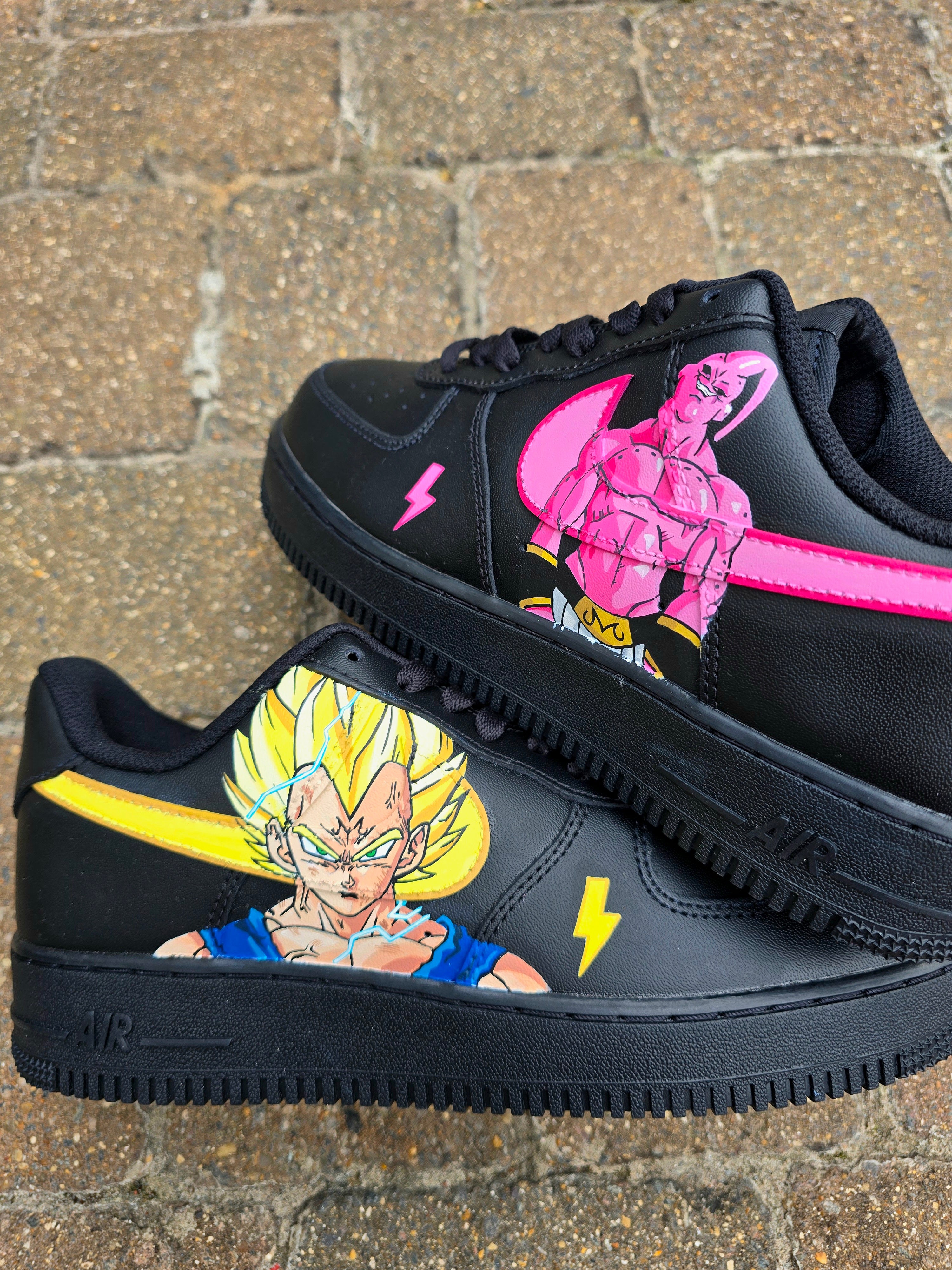 Custom Dragon Ball Z Nike Air Force 1 sneakers featuring hand-painted anime artwork of Majin Buu and Super Saiyan Goku. Black leather base with pink and yellow accents, lightning bolt details, and high-quality, waterproof custom paint job.


