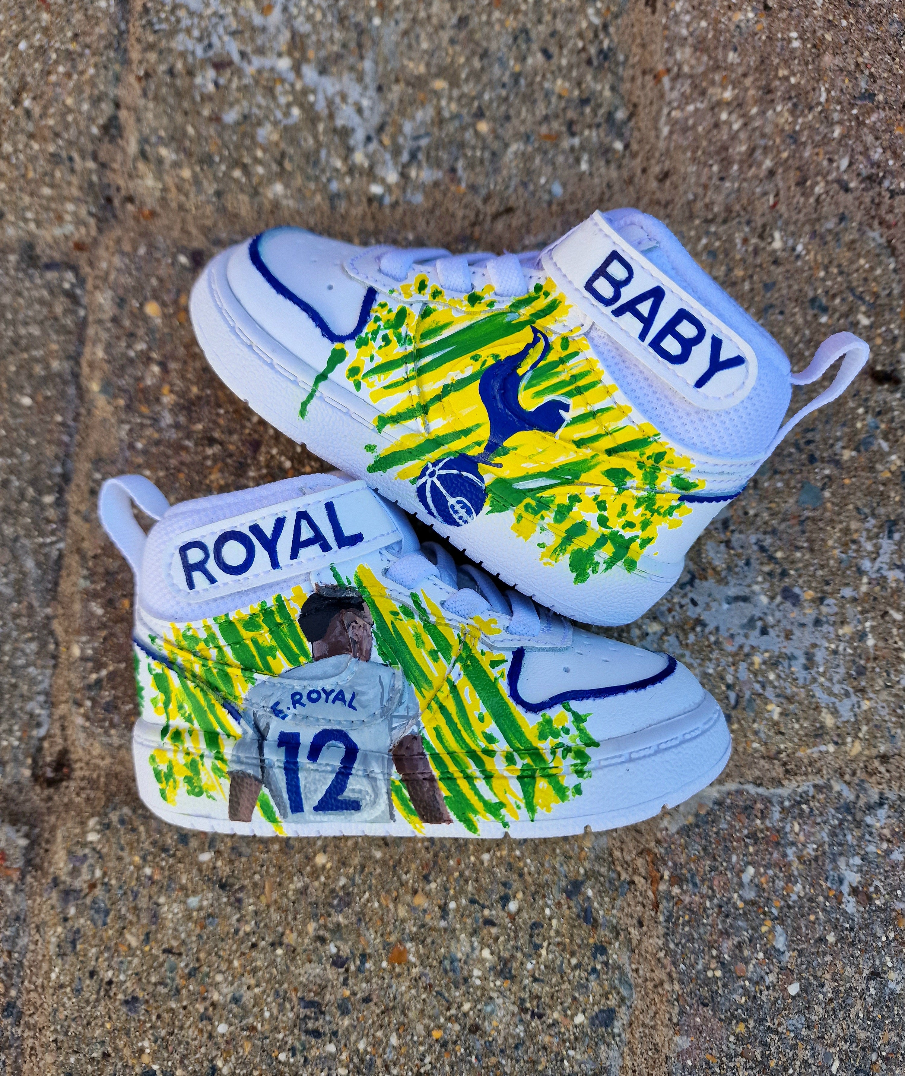 Custom hand-painted baby Adidas sneakers inspired by Brazilian footballer Emerson Royal. Features toddler-sized high-top shoes with illustrations of Emerson in Spurs and Brazil kits, Brazil flag background, colorful 3-stripes, and "Emerson Royal" detailing on the heel. Designed for toddlers, crafted with non-toxic paint, and finished with vibrant detailing by Gitartsy.

