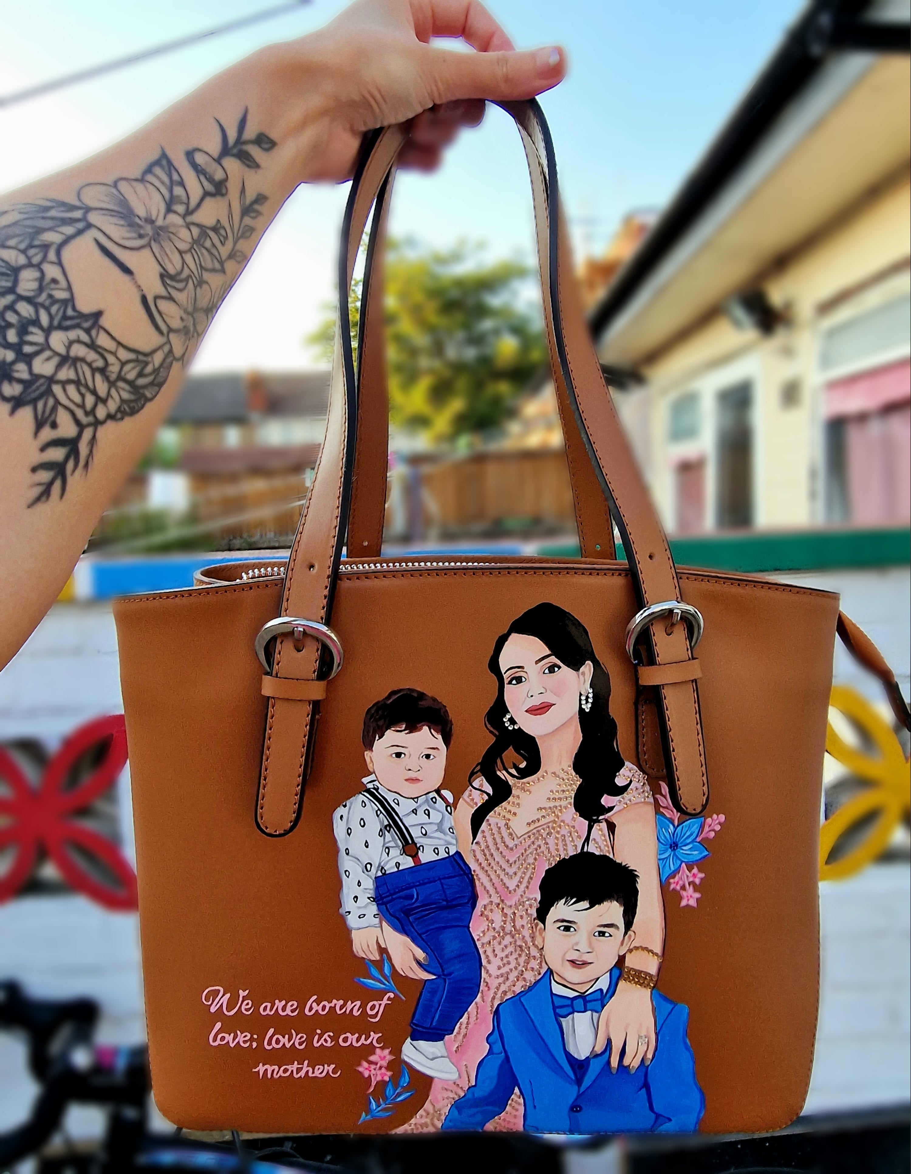 A custom hand-painted tan leather tote bag featuring a family portrait of a mother and two children, designed in a detailed artistic style with floral embellishments and a heartfelt quote. This unique leather bag is personalized from your photos and painted using durable, waterproof paints, ideal as a memory keepsake or meaningful gift for mothers. The painted design stands out against the rich tan leather, making it both functional and sentimental.

