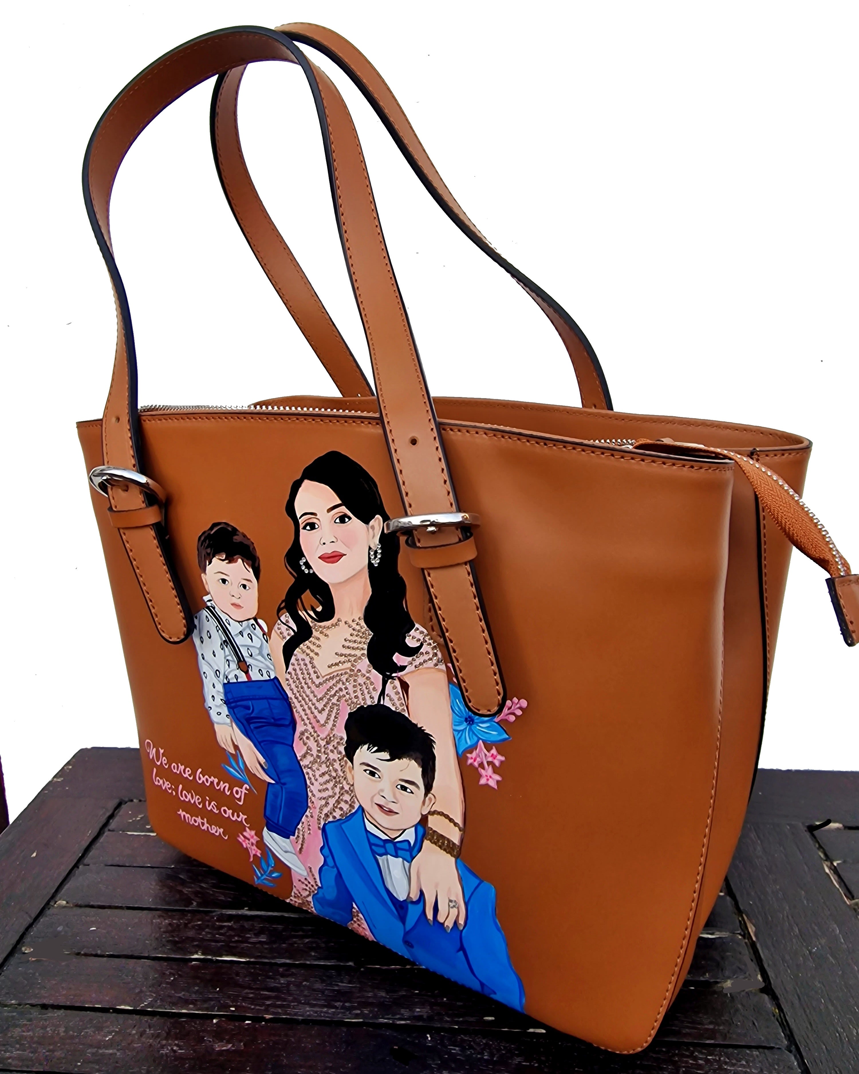 A custom hand-painted tan leather tote bag featuring a family portrait of a mother and two children, designed in a detailed artistic style with floral embellishments and a heartfelt quote. This unique leather bag is personalized from your photos and painted using durable, waterproof paints, ideal as a memory keepsake or meaningful gift for mothers. The painted design stands out against the rich tan leather, making it both functional and sentimental.

