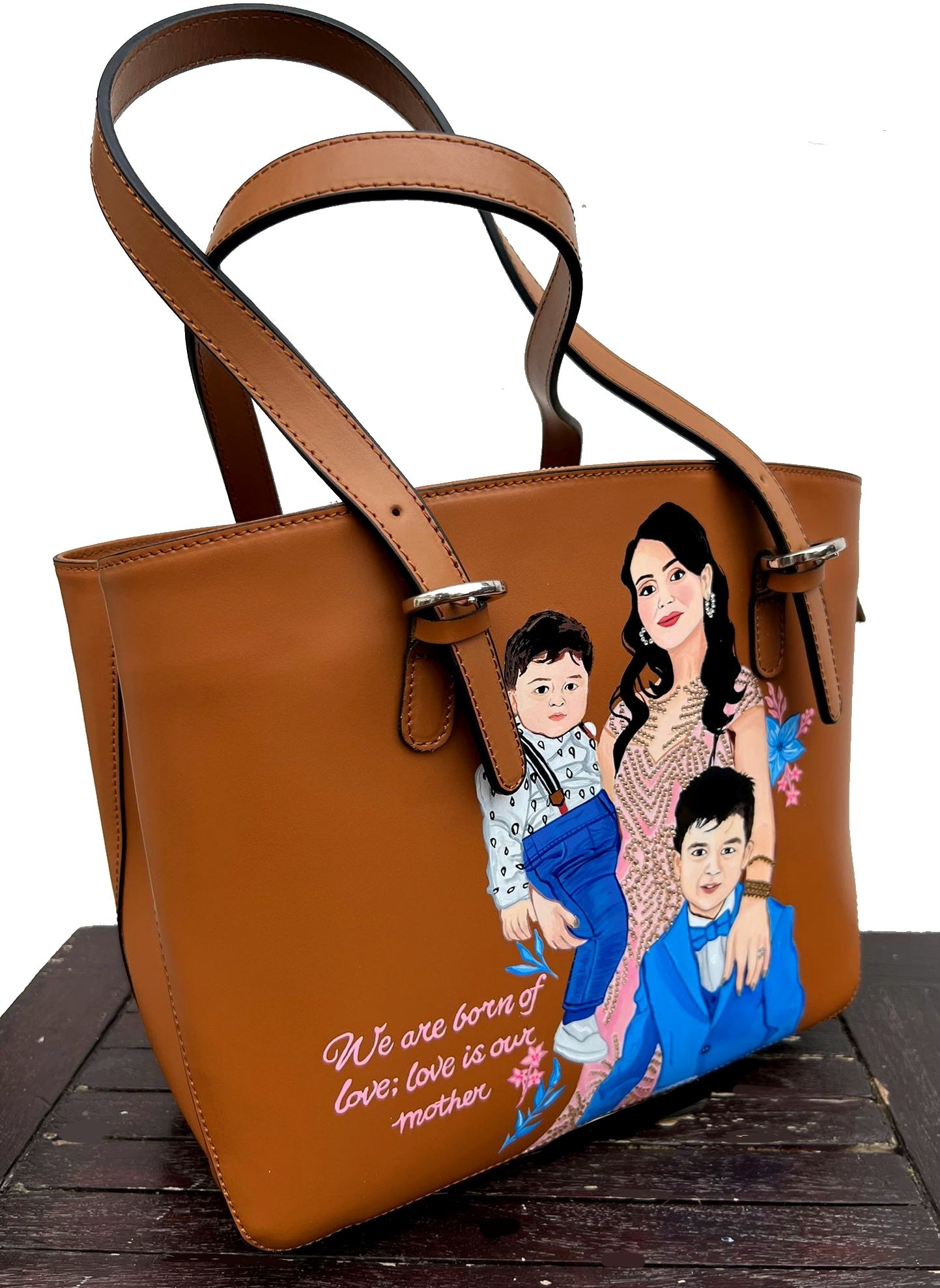 A custom hand-painted tan leather tote bag featuring a family portrait of a mother and two children, designed in a detailed artistic style with floral embellishments and a heartfelt quote. This unique leather bag is personalized from your photos and painted using durable, waterproof paints, ideal as a memory keepsake or meaningful gift for mothers. The painted design stands out against the rich tan leather, making it both functional and sentimental.

