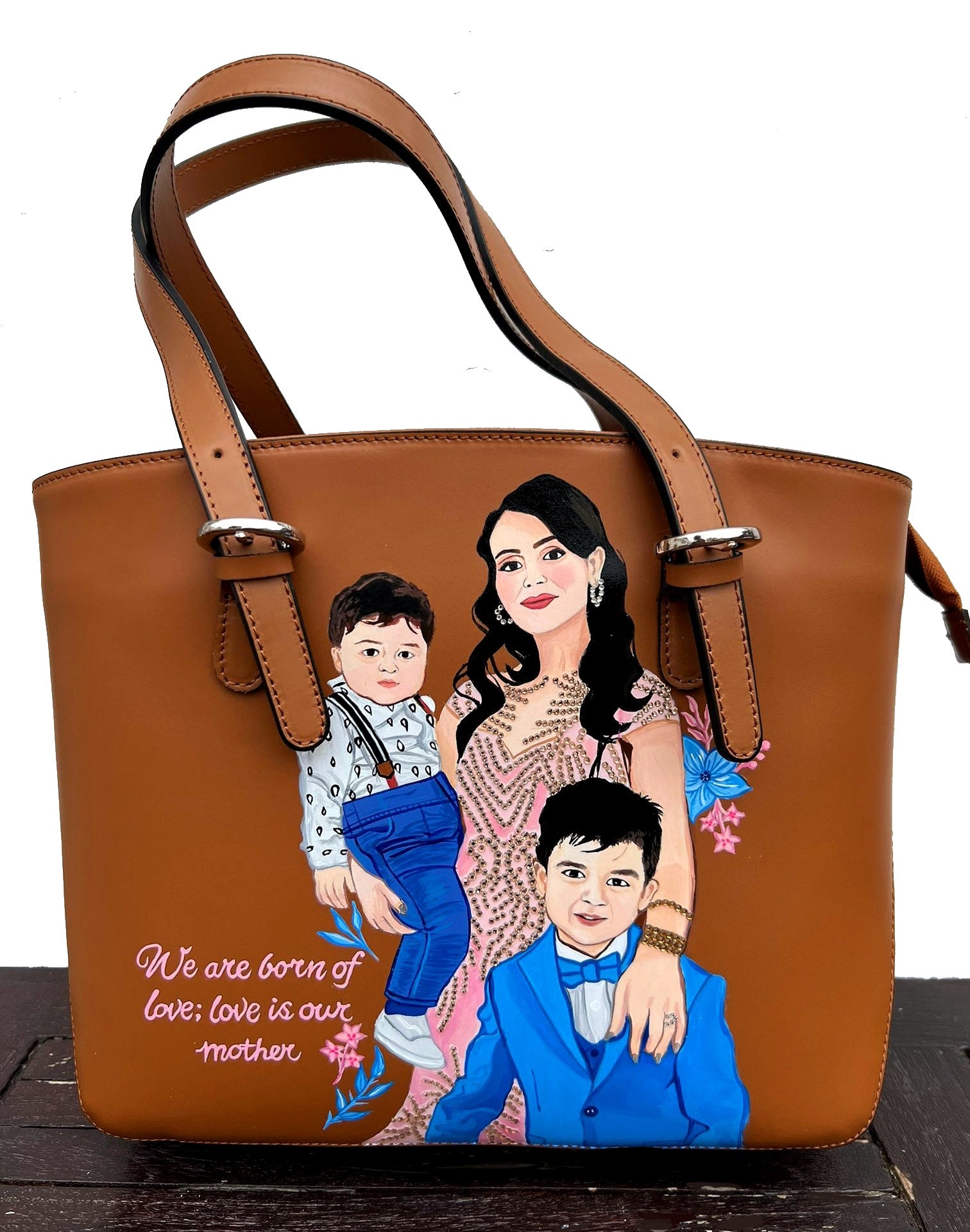 A custom hand-painted tan leather tote bag featuring a family portrait of a mother and two children, designed in a detailed artistic style with floral embellishments and a heartfelt quote. This unique leather bag is personalized from your photos and painted using durable, waterproof paints, ideal as a memory keepsake or meaningful gift for mothers. The painted design stands out against the rich tan leather, making it both functional and sentimental.


