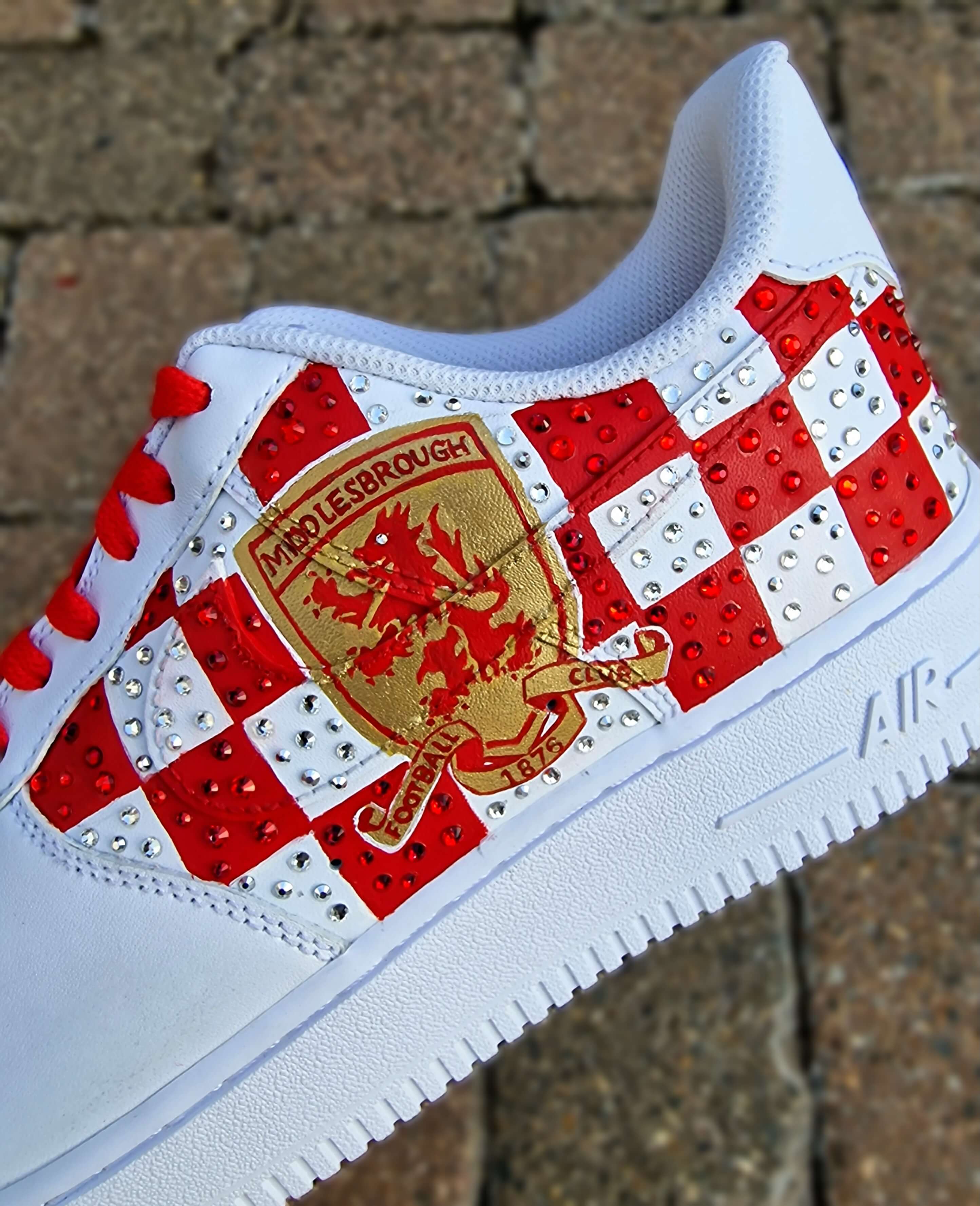 Custom hand-painted sneakers featuring Middlesbrough FC crest, red-and-white checkered pattern with stud embellishments, and detailed Riverside Stadium artwork. White base sneakers with red laces, designed by Gitartsy for football fans, sneaker collectors, and Boro supporters.

