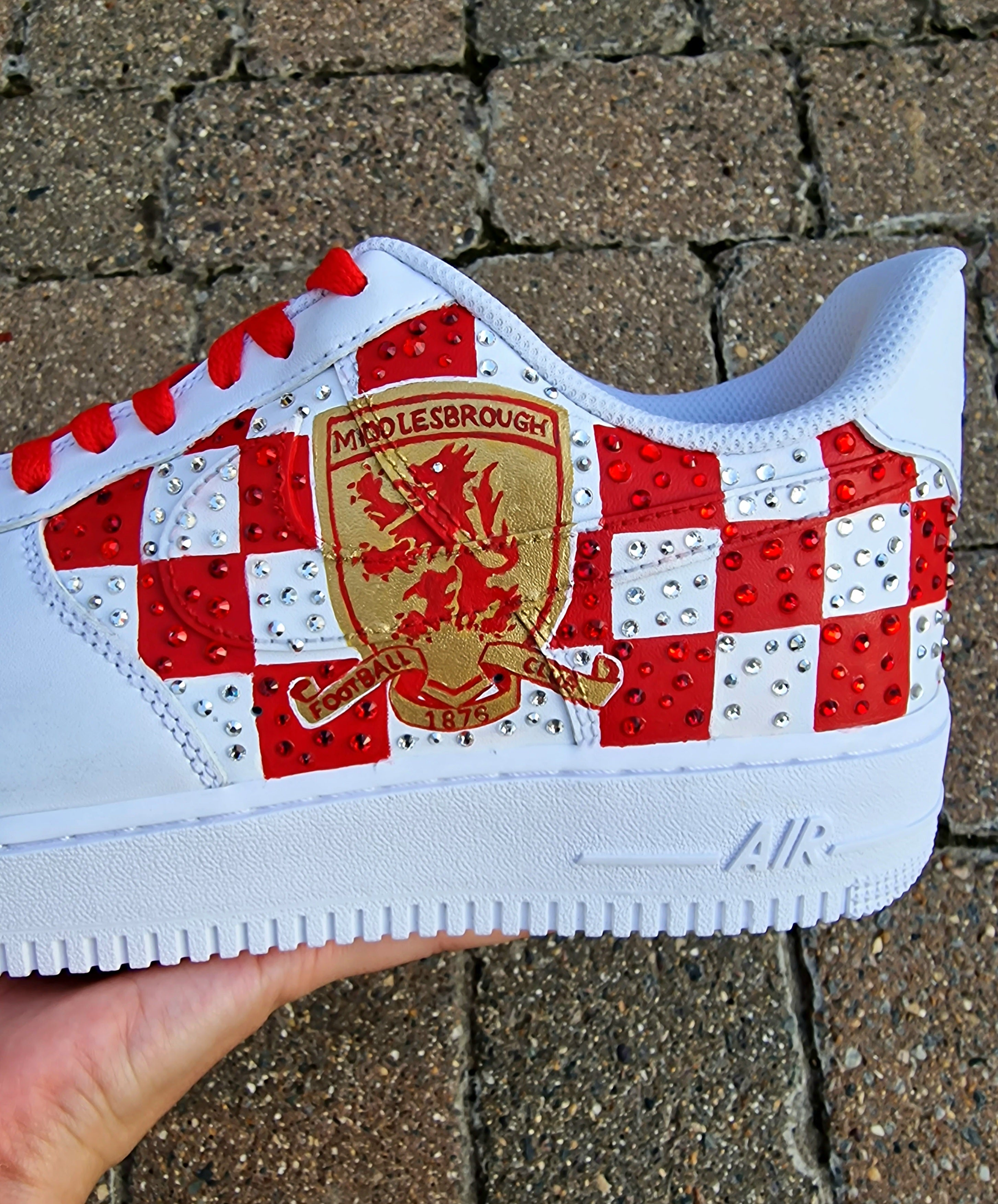 Custom hand-painted sneakers featuring Middlesbrough FC crest, red-and-white checkered pattern with stud embellishments, and detailed Riverside Stadium artwork. White base sneakers with red laces, designed by Gitartsy for football fans, sneaker collectors, and Boro supporters.

