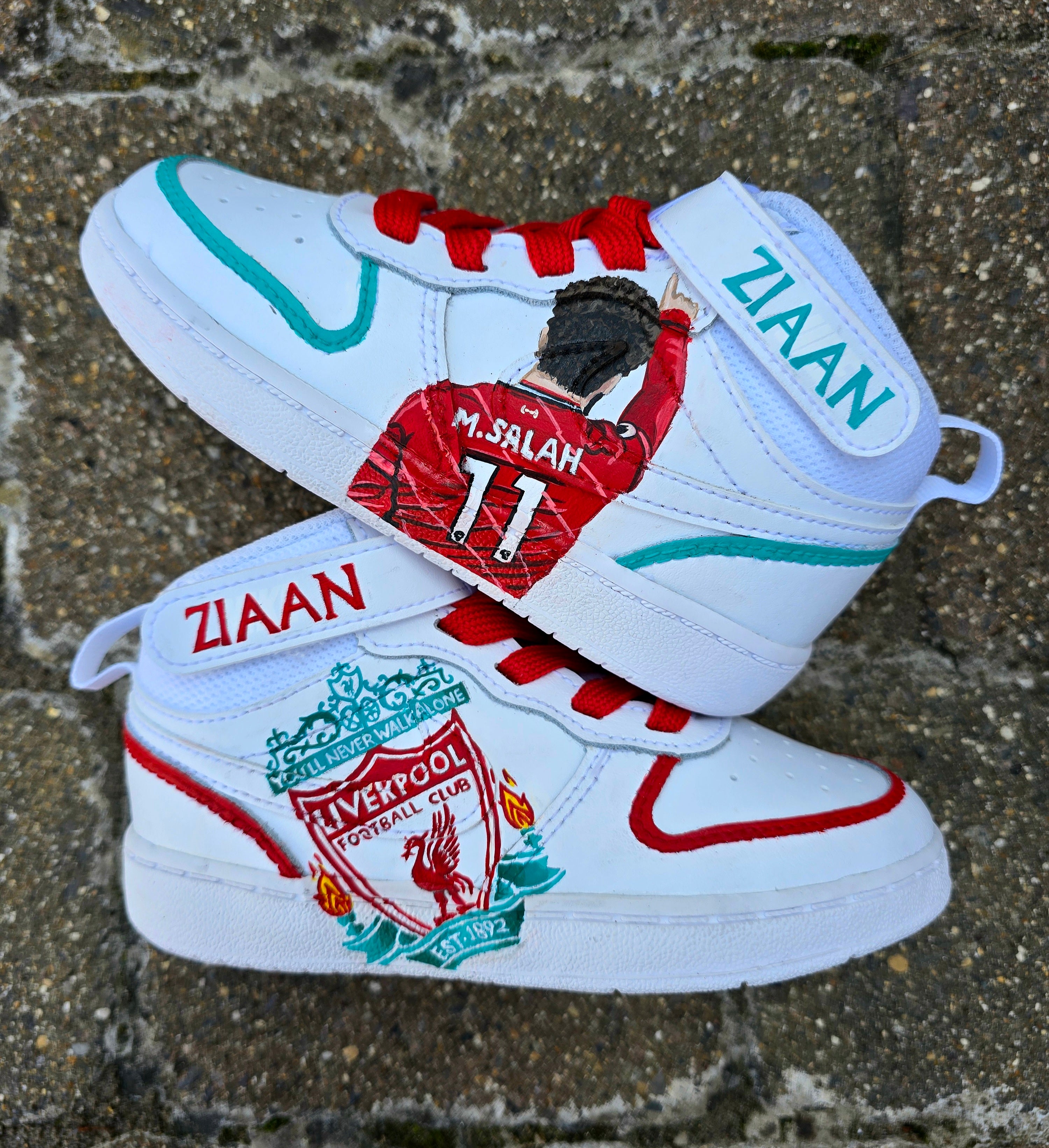 Hand-painted custom baby sneakers featuring a Liverpool FC theme with Mo Salah portrait and club crest. Personalized toddler shoes with red and teal accents, bright red laces, and your child’s name on the Velcro strap. Unique wearable artwork by Gitartsy.