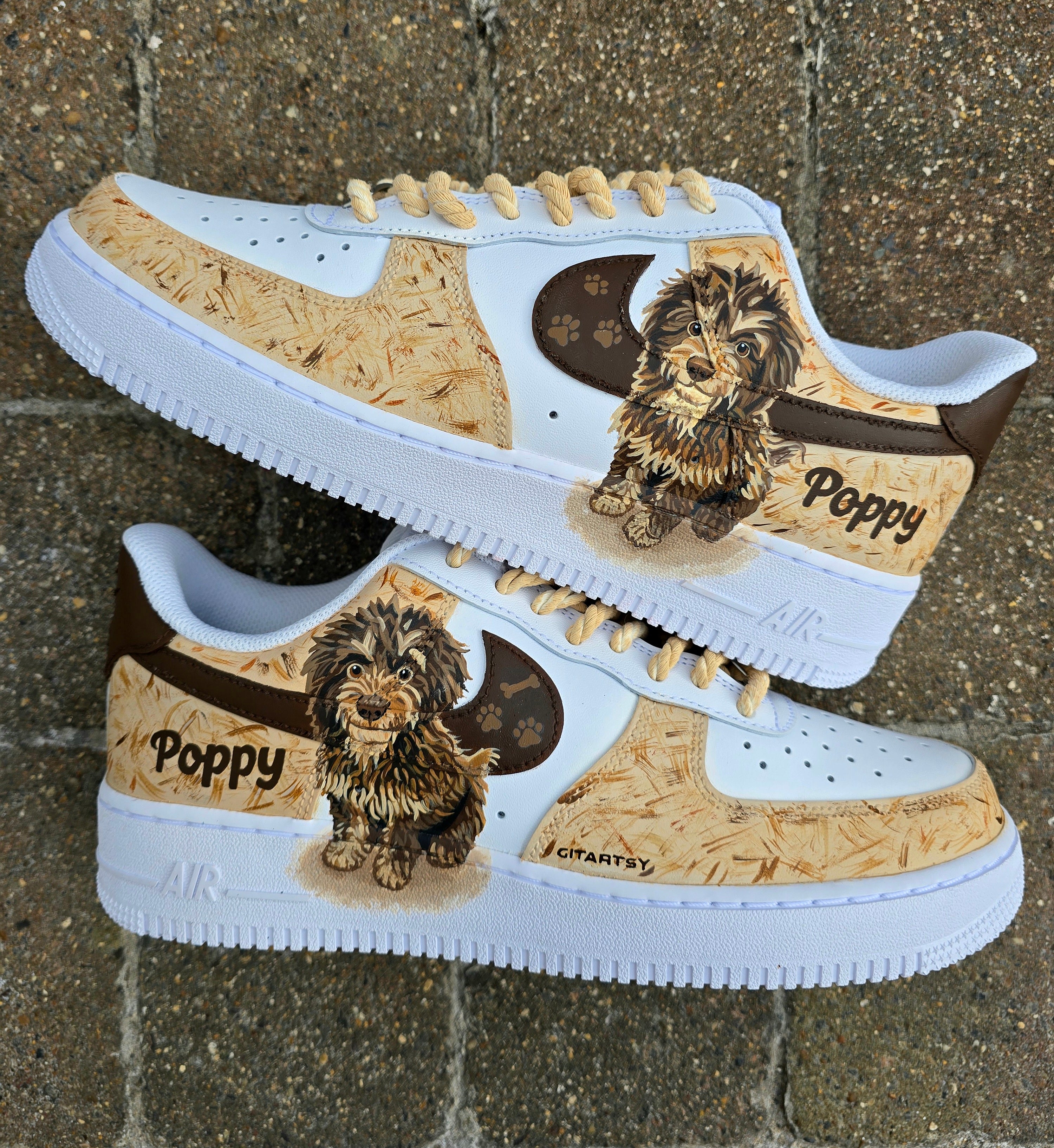 Custom hand-painted Nike Air Force 1 sneakers featuring a detailed portrait of a fluffy brown dog named Poppy 🐶. The shoes have a white leather base with light brown textured paint accents and a rich chocolate-brown swoosh adorned with paw prints 🐾. The pet’s name is written in a playful font, and tan rope laces add a rustic touch. Perfect for showcasing love for your pet in a stylish and artistic way.

