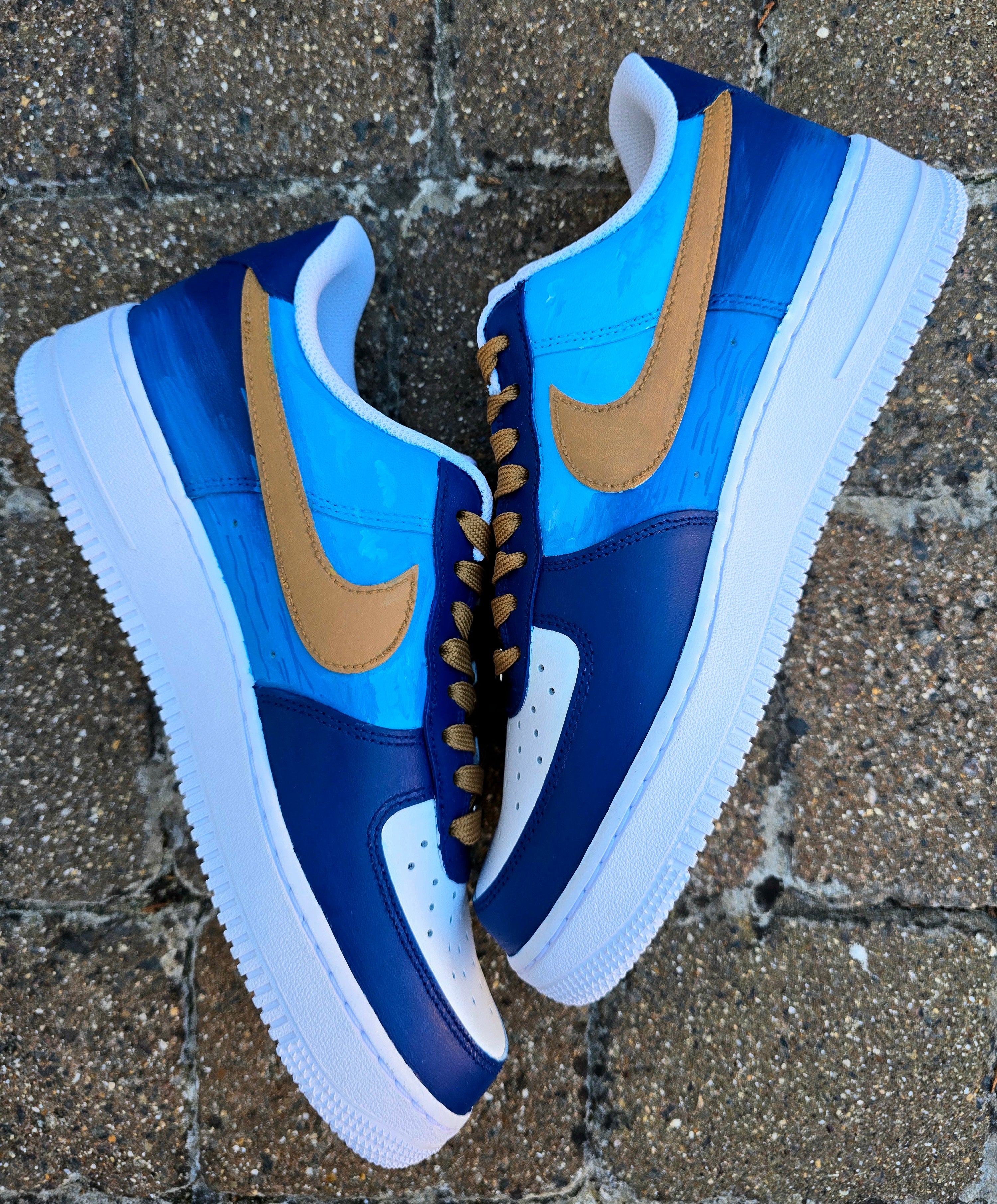 Custom Nike Air Force 1 sneakers 🐾 hand-painted with a detailed toy poodle pet portrait, featuring a caramel-colored curly-haired dog sitting in a grassy field with a blue sky and lake background. Includes the pet’s name in stylish script, paw prints, bones, and heart icons, all painted on a blue and navy color-block base with golden-brown laces. Each pair is personalized to match your pet’s likeness and crafted using durable, waterproof leather paints, making them wearable art for dog lovers.

