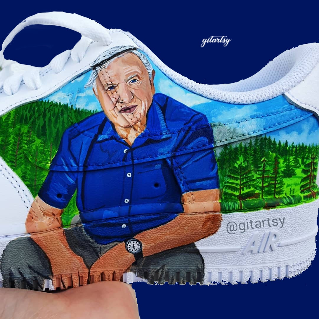 Custom hand-painted Nike Air Force 1 sneakers featuring a detailed portrait of David Attenborough seated in a lush natural forest landscape. The background includes vibrant green trees and blue skies, painted across the shoe panels. Crafted by Gitartsy, these sneakers are a tribute to nature, sustainability, and the legendary naturalist, using premium acrylic paints and sealed for durability.

