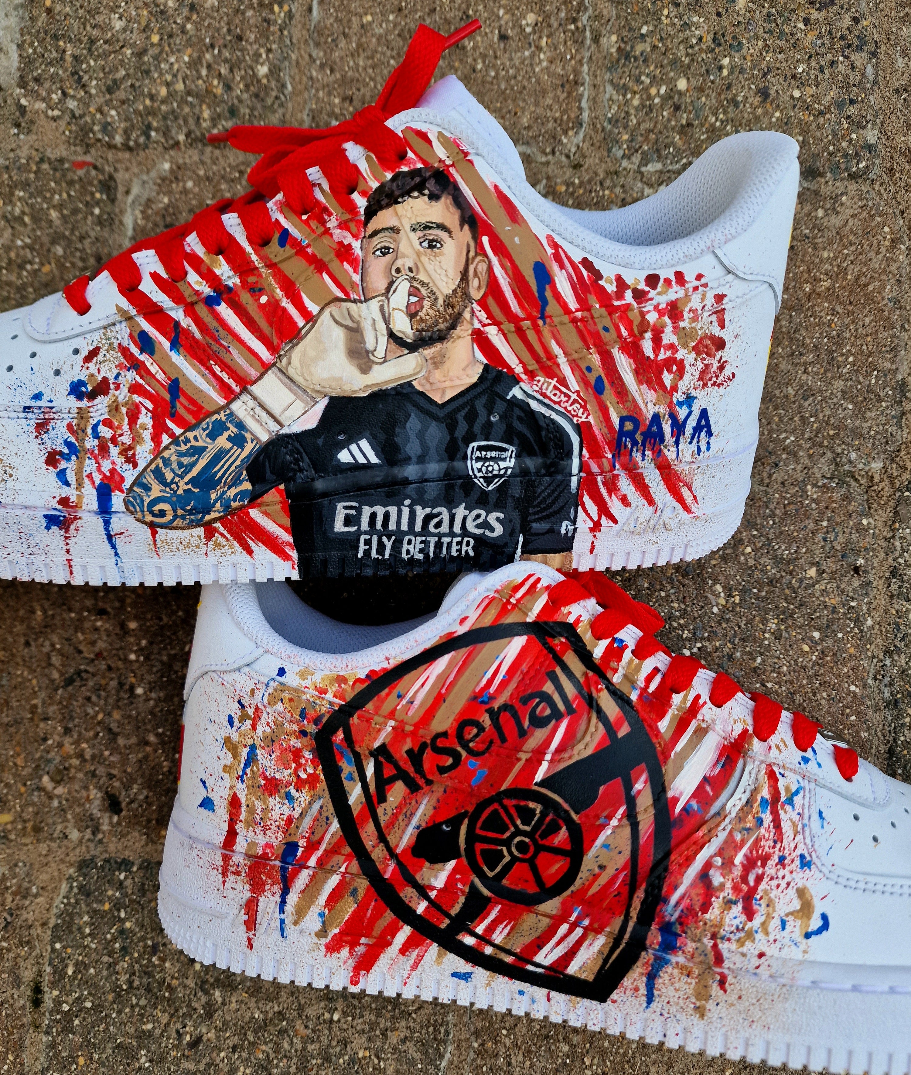 Hand-painted custom Nike Air Force 1 sneakers featuring David Raya in Arsenal goalkeeper kit, Arsenal crest, Spanish flag and colors, vibrant football-inspired splatter artwork, crafted by Gitartsy.

