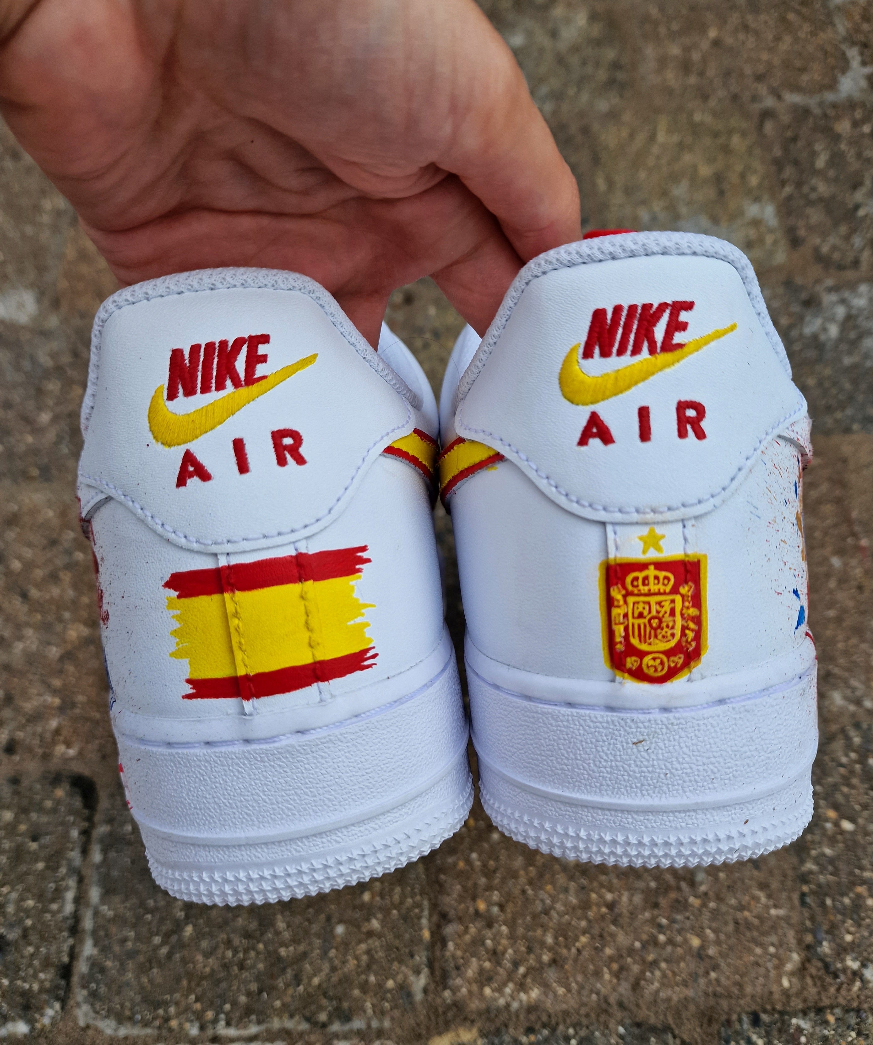 Hand-painted custom Nike Air Force 1 sneakers featuring David Raya in Arsenal goalkeeper kit, Arsenal crest, Spanish flag and colors, vibrant football-inspired splatter artwork, crafted by Gitartsy.

