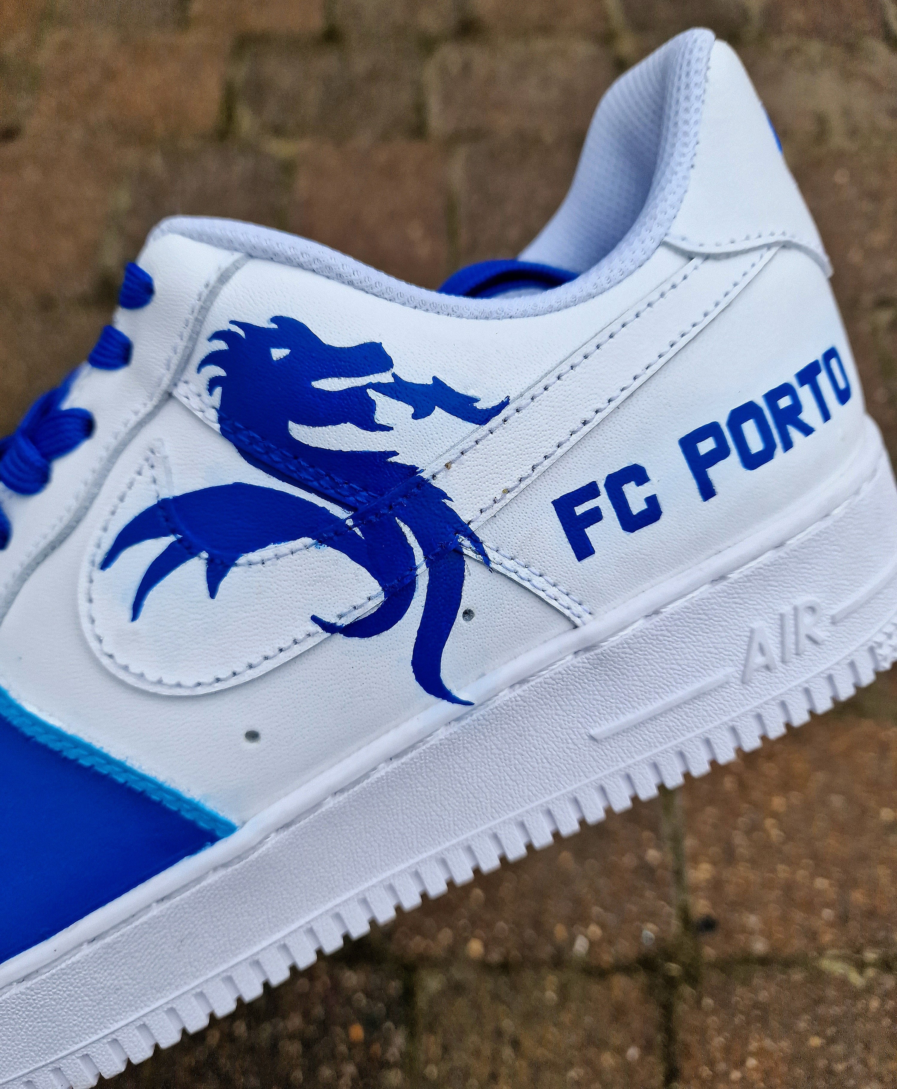 Custom FC Porto Nike Air Force 1 sneakers designed for football fans, featuring hand-painted artwork with the official club crest, blue and white color scheme, dragon mascot, and player number detailing. These one-of-a-kind shoes are crafted using authentic Nike AF1s and painted with weather-resistant leather paints. Perfect for sports lovers and collectors, combining comfort with team spirit.

