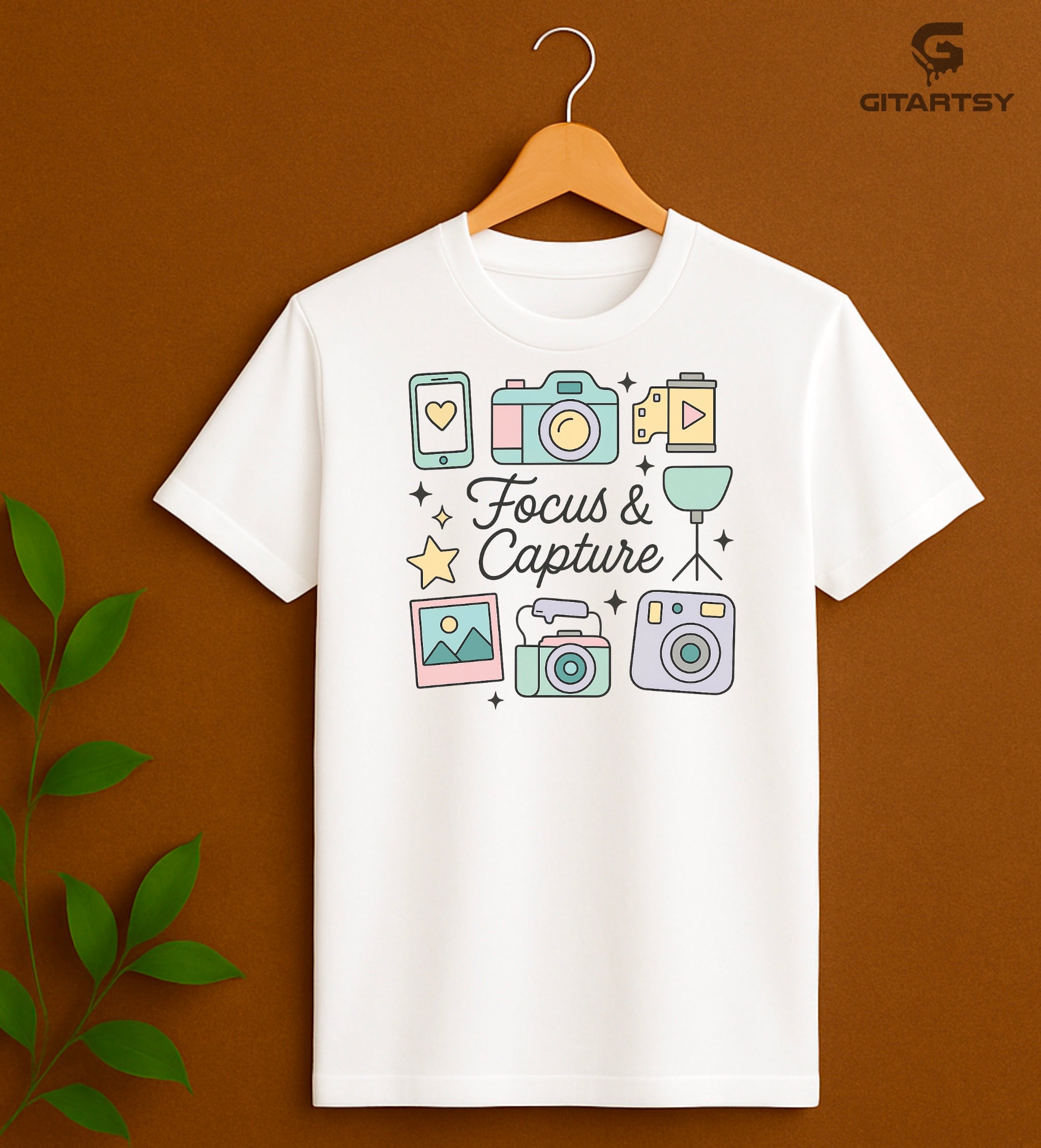 Pastel aesthetic "Focus & Capture" graphic T-shirt for photographers and videographers, featuring illustrated cameras, tripod, polaroid, smartphone, and video icons on a soft cotton tee in neutral and pastel shades.
