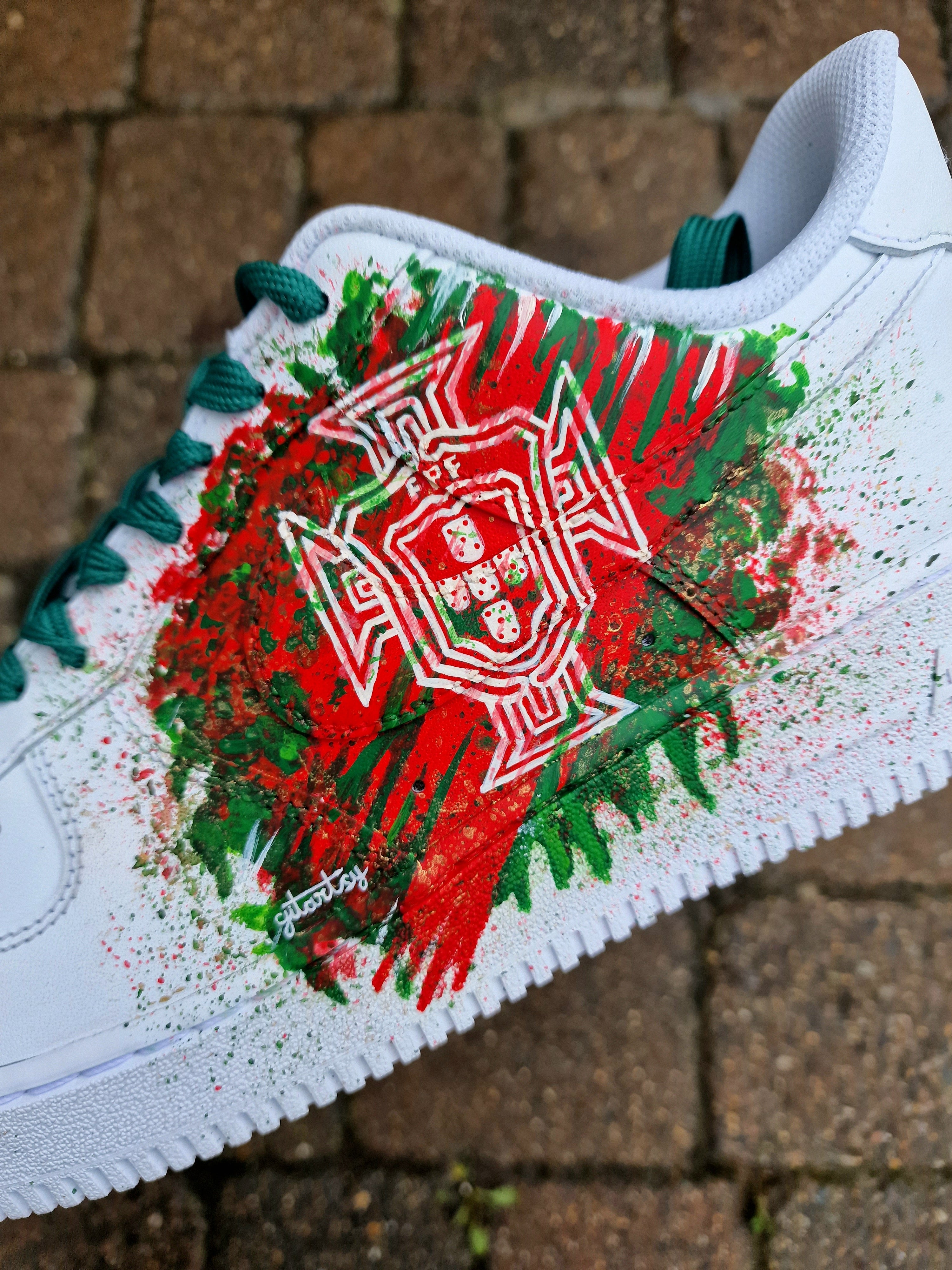 "Custom hand-painted Nike Air Force 1 sneakers featuring Manchester United and Portugal national football team crests, splattered in bold red, green, and black paint with unique details, crafted by Gitartsy."

