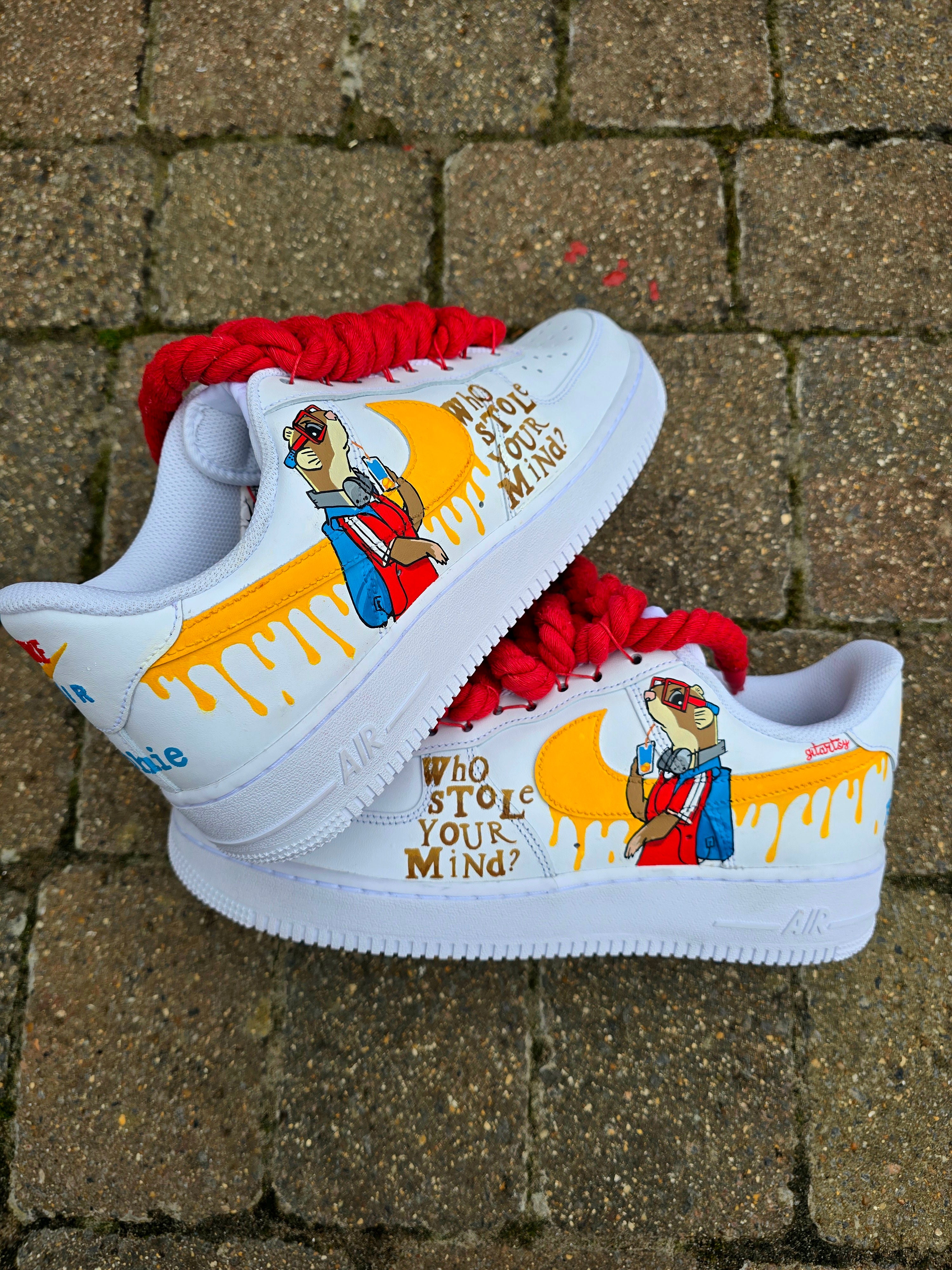 Custom hand-painted Nike Air Force 1 sneakers featuring unique cartoon artwork inspired by the book Who Stole Your Mind? by Being Alphie. The shoes showcase vibrant illustrations, bright yellow swoosh drips, thick red rope laces, and hand-lettered text on premium leather for book lovers, art collectors, and streetwear fans.

