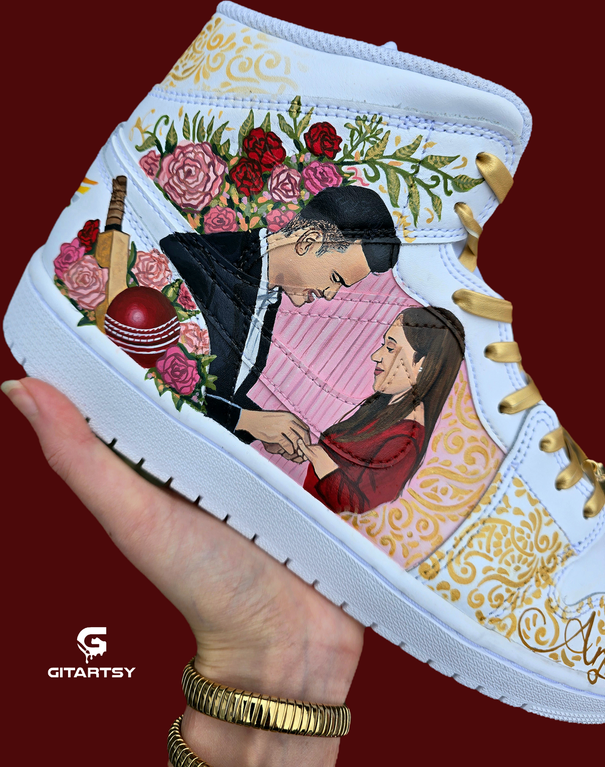 A pair of nike jordan 1 white high-top sneakers with custom illustrations of a couple Arjun Tendulkar and Saaniya Chandhok with gold paisley patterns henna, pets, florals with maroon and blue colour scheme displayed against a dark red background with a GITARTSY logo in the corner.