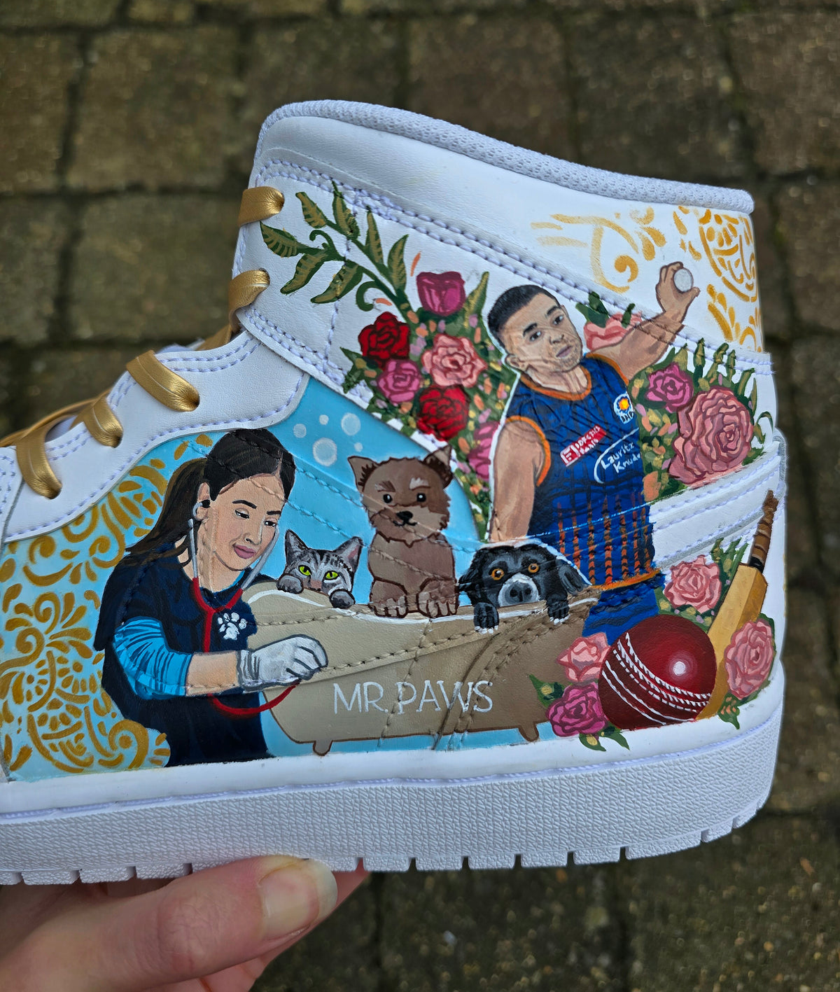 A pair of nike jordan 1 white high-top sneakers with custom illustrations of a couple Arjun Tendulkar and Saaniya Chandhok with gold paisley patterns henna, pets, florals with maroon and blue colour scheme displayed against a dark red background with a GITARTSY logo in the corner.