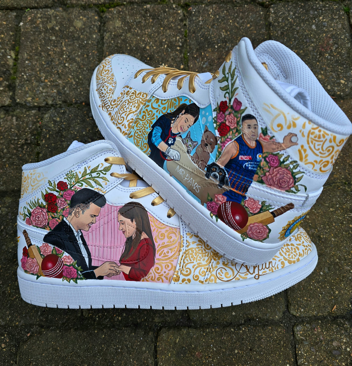 A pair of nike jordan 1 white high-top sneakers with custom illustrations of a couple Arjun Tendulkar and Saaniya Chandhok with gold paisley patterns henna, pets, florals with maroon and blue colour scheme displayed against a dark red background with a GITARTSY logo in the corner.
