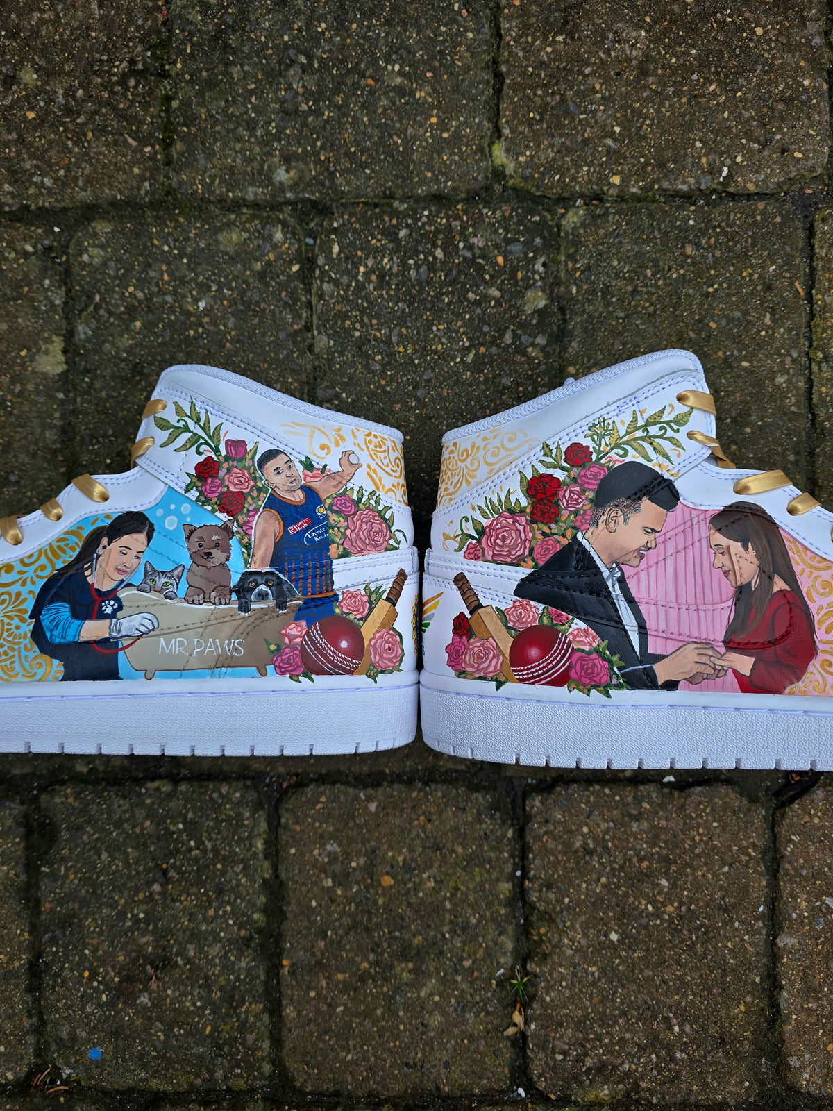 A pair of nike jordan 1 white high-top sneakers with custom illustrations of a couple Arjun Tendulkar and Saaniya Chandhok with gold paisley patterns henna, pets, florals with maroon and blue colour scheme displayed against a dark red background with a GITARTSY logo in the corner.