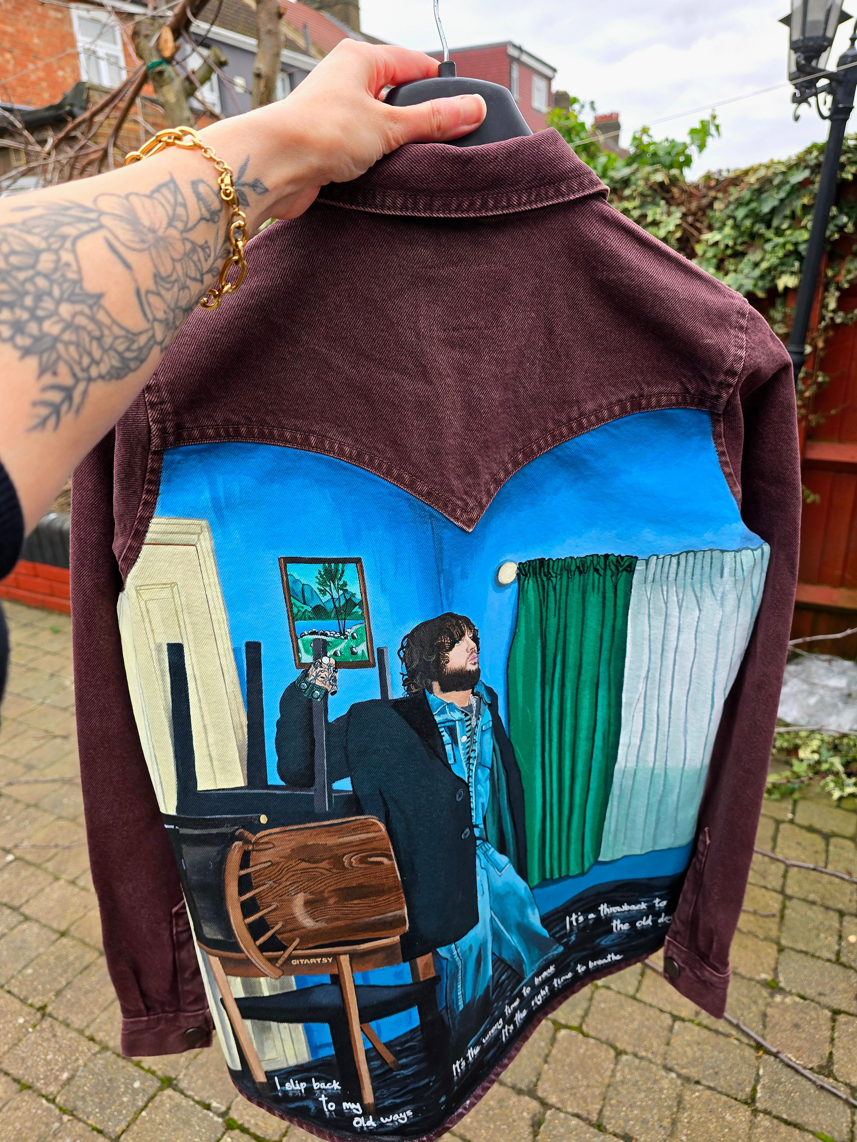 James Arthur Singer Hand Painted Denim Jacket featuring a detailed back artwork of James Arthur in a vibrant indoor scene, painted on a burgundy denim jacket with “Pisces” embroidered on the front, created by Gitartsy using high-quality fabric paints for long-lasting wear.

