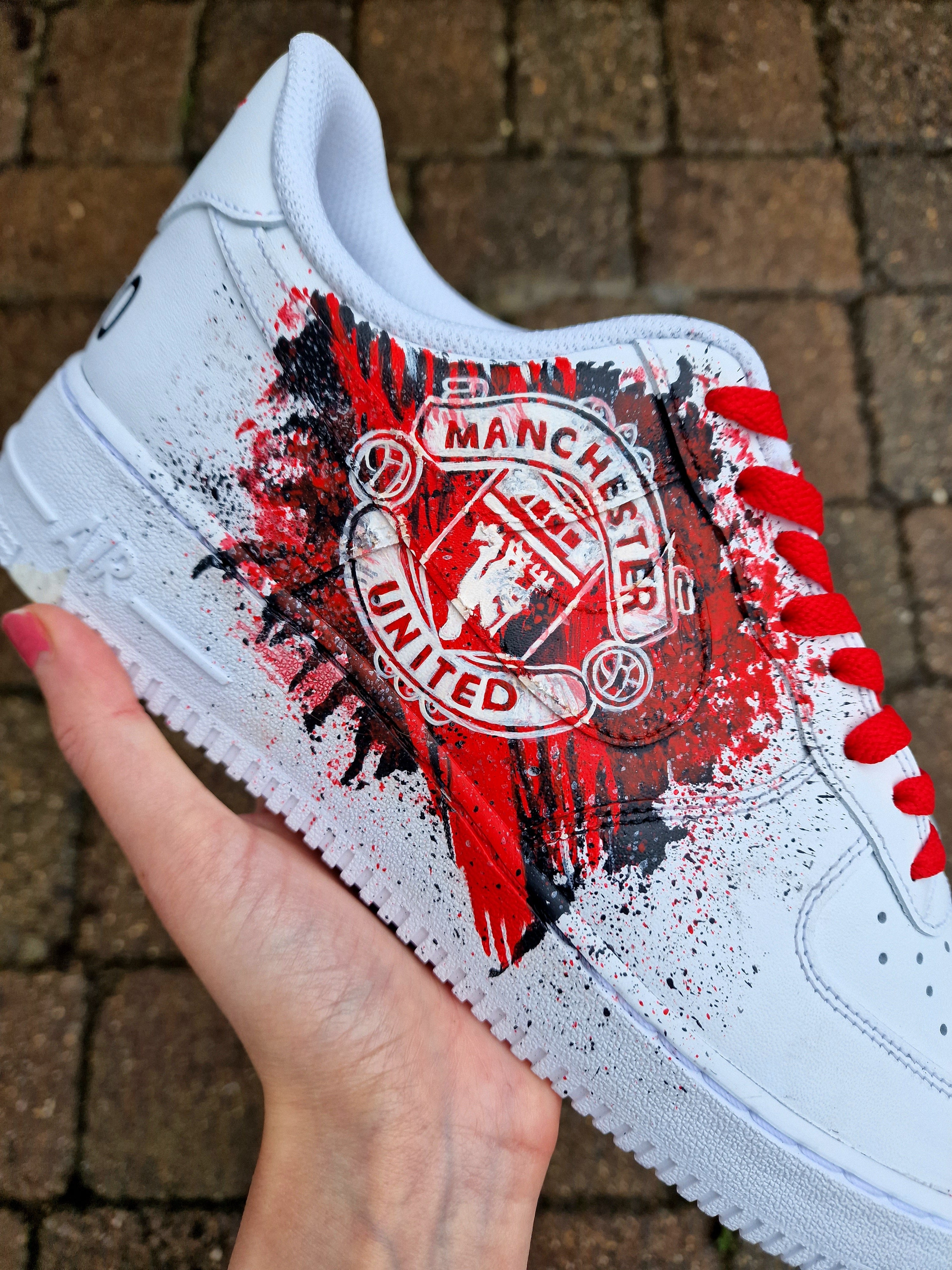 "Custom hand-painted Nike Air Force 1 sneakers featuring Manchester United and Portugal national football team crests, splattered in bold red, green, and black paint with unique details, crafted by Gitartsy."

