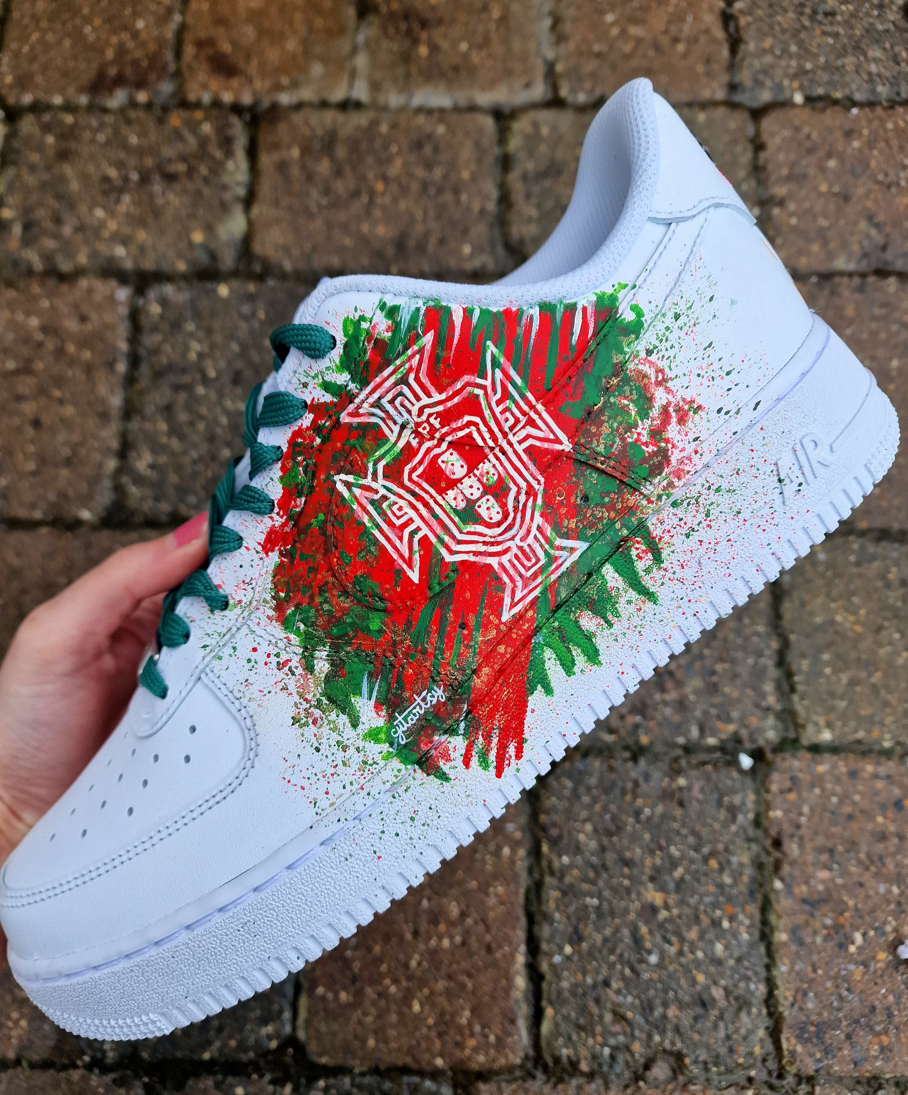 "Custom hand-painted Nike Air Force 1 sneakers featuring Manchester United and Portugal national football team crests, splattered in bold red, green, and black paint with unique details, crafted by Gitartsy."

