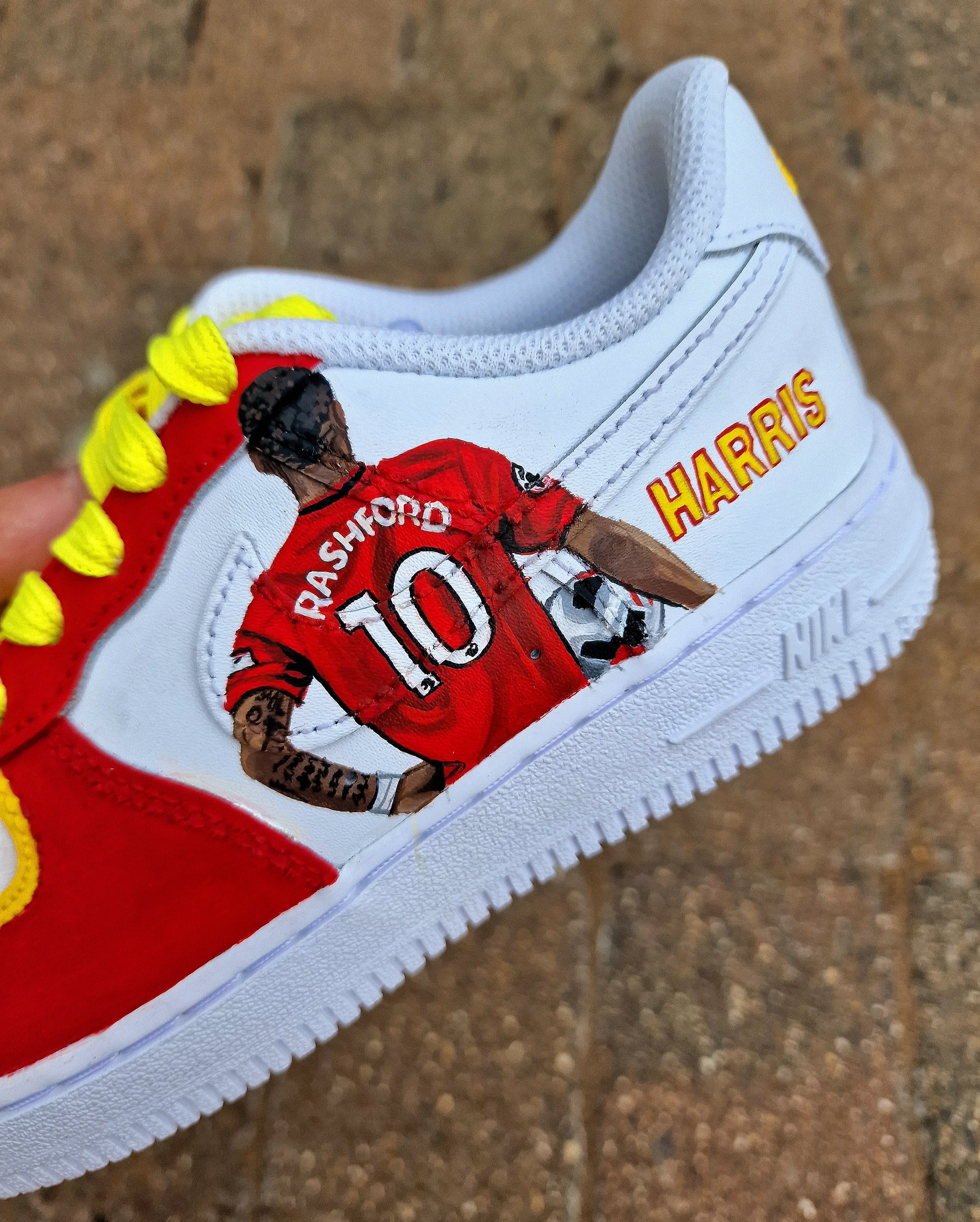Hand-painted custom sneakers featuring the Manchester United crest, Marcus Rashford kit illustration, and personalized details on a red, yellow, and white theme; perfect for football fans.

